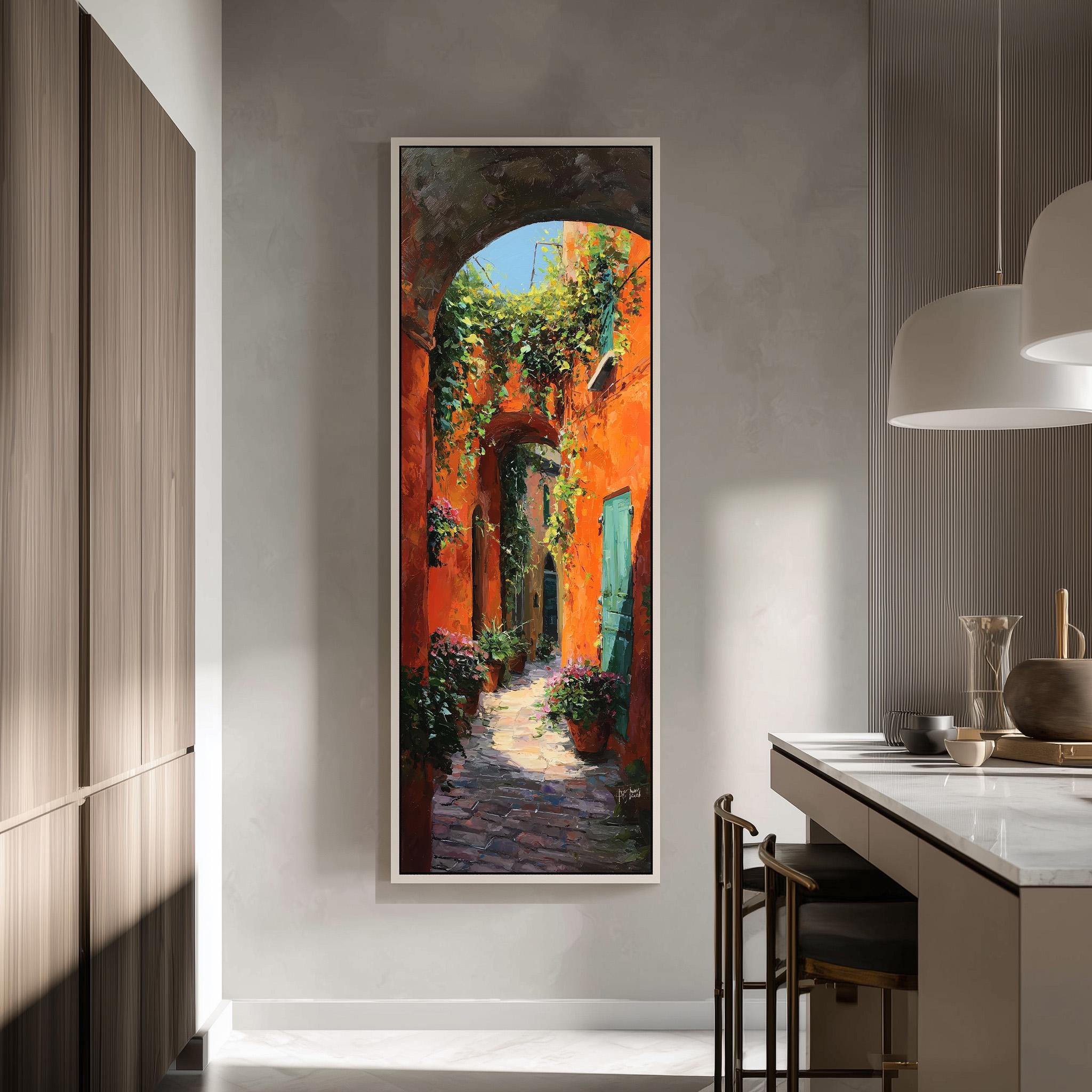 a large, colorful painting of a narrow alleyway with a stone path, surrounded by orange walls and green plants. The painting is hung on a wall in a modern kitchen with a countertop and chairs.