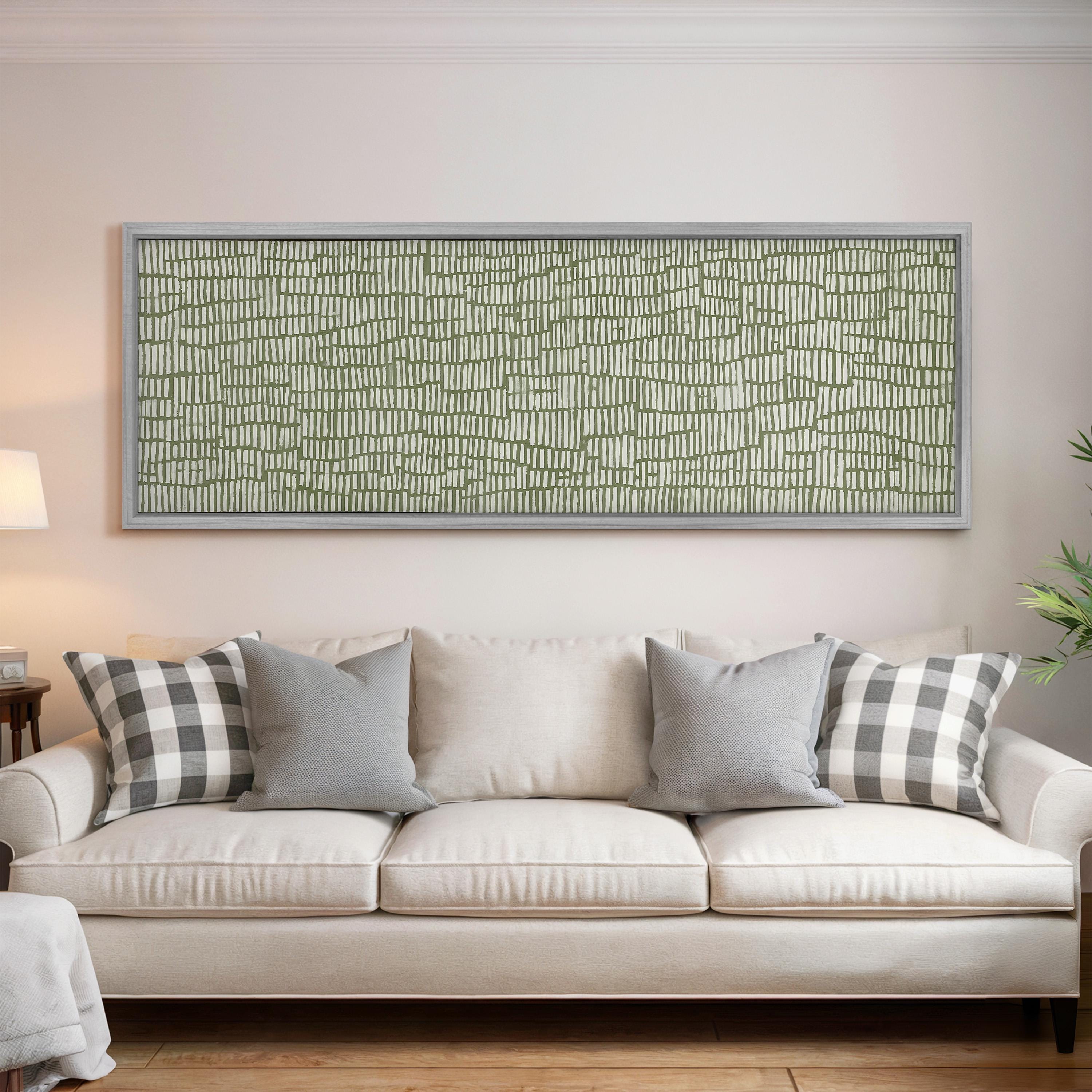 a living room with a white sofa adorned with gray and white patterned throw pillows. Above the sofa, there is a large framed artwork with a green and white geometric pattern.