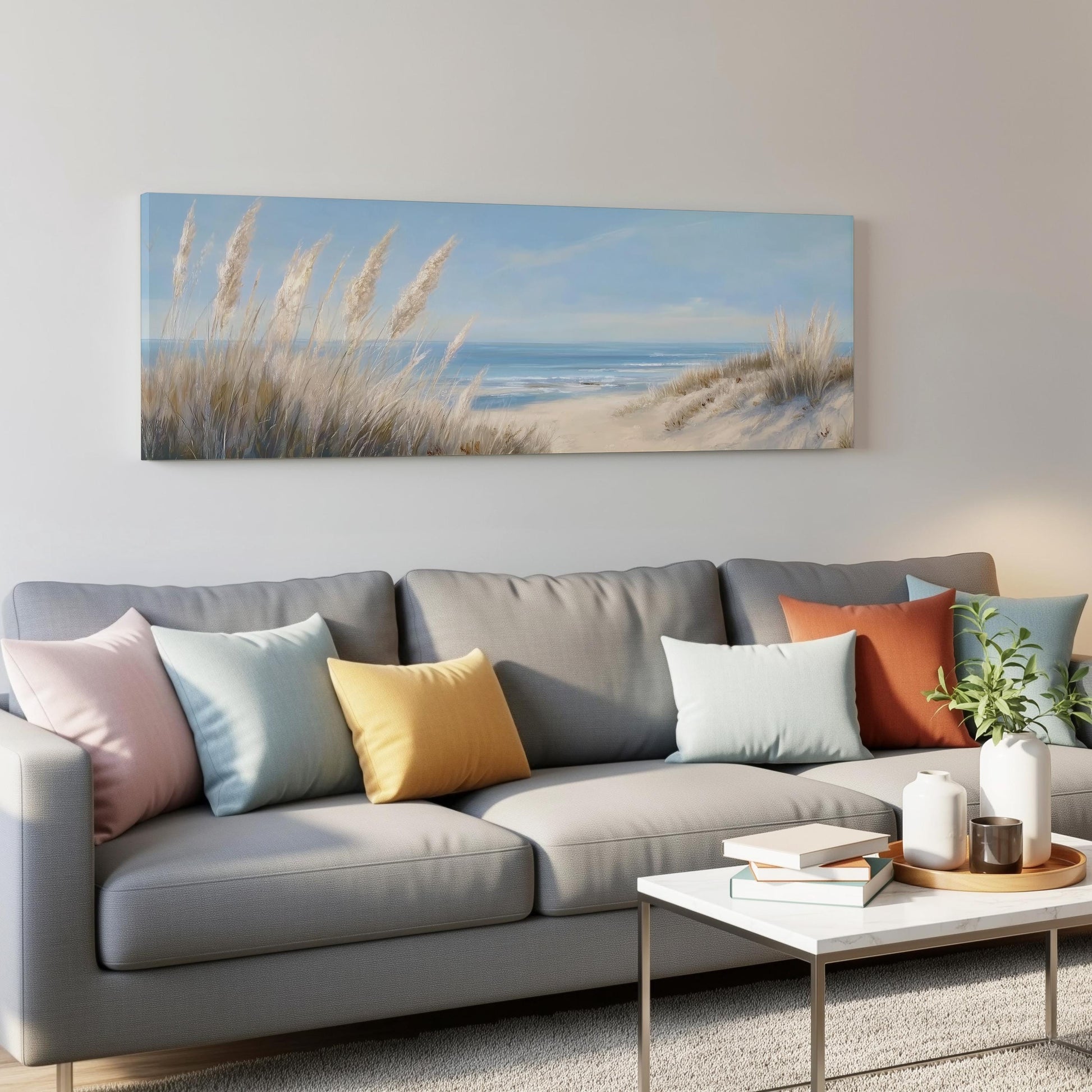 a living room with a gray sofa adorned with colorful throw pillows, a white coffee table, and a painting of a beach scene hanging on the wall above the sofa.