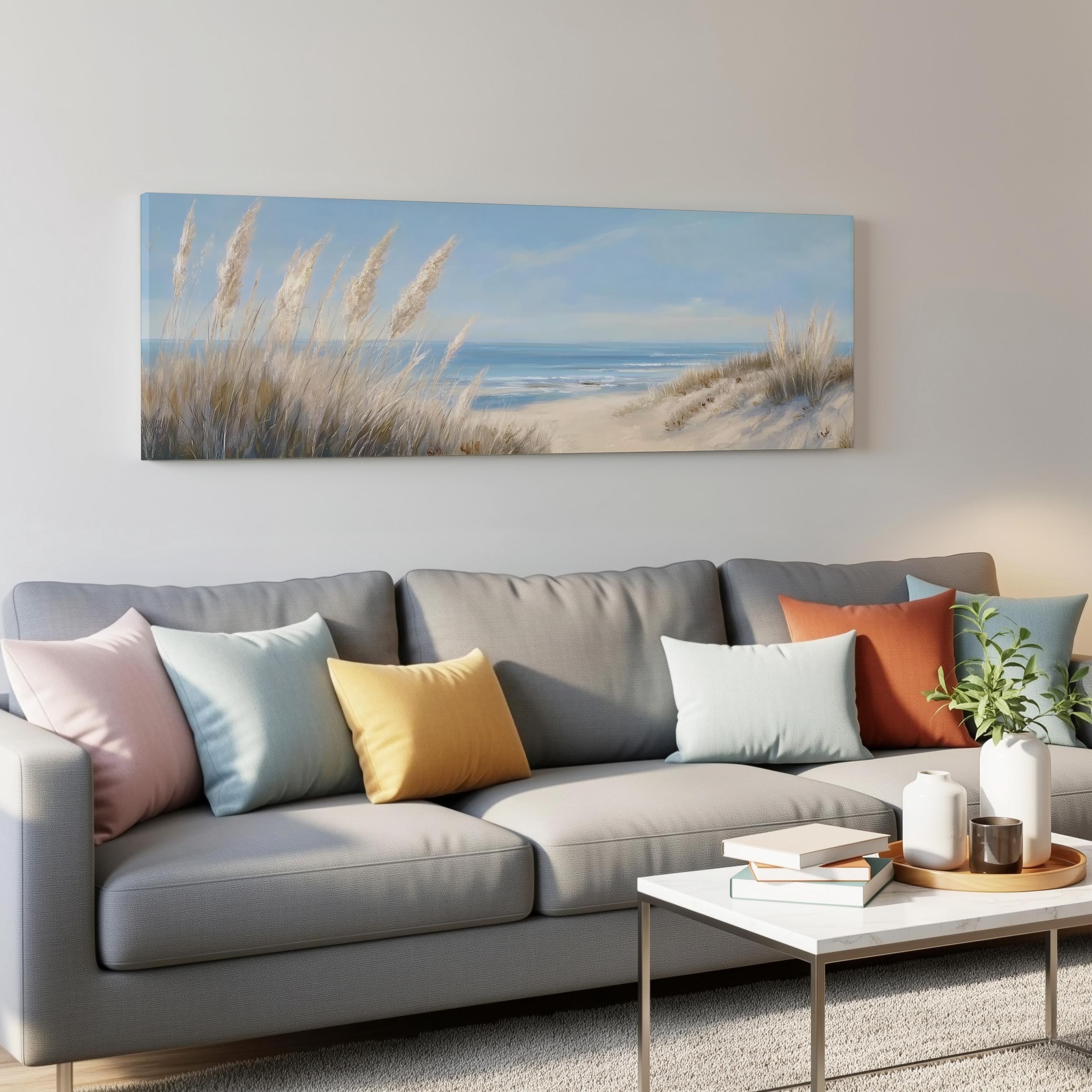 a living room with a gray sofa adorned with colorful throw pillows, a white coffee table, and a painting of a beach scene hanging on the wall above the sofa.