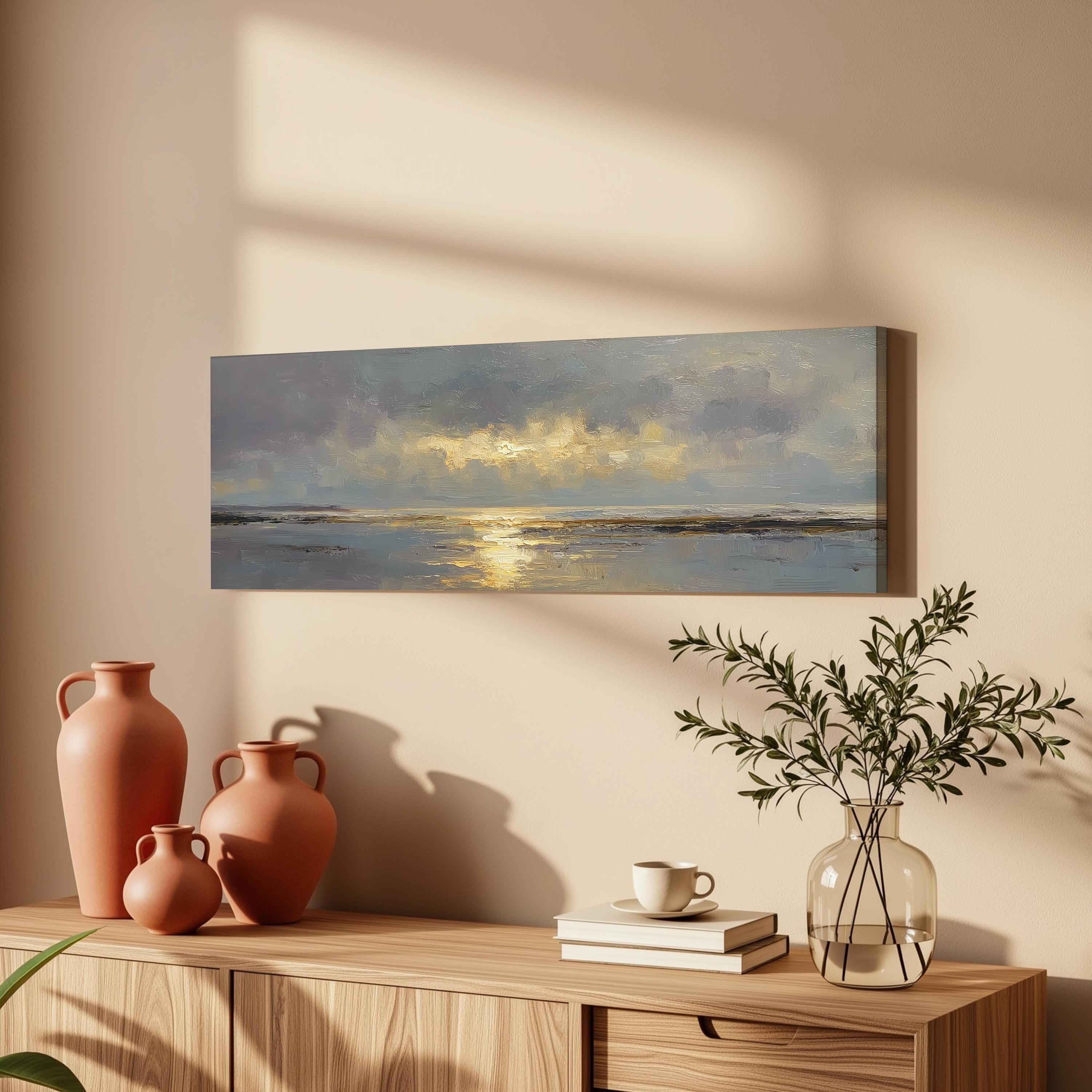 a wooden cabinet with a painting of a serene landscape hanging on the wall above it. The cabinet also displays three orange vases, a glass vase with greenery, and a stack of books.