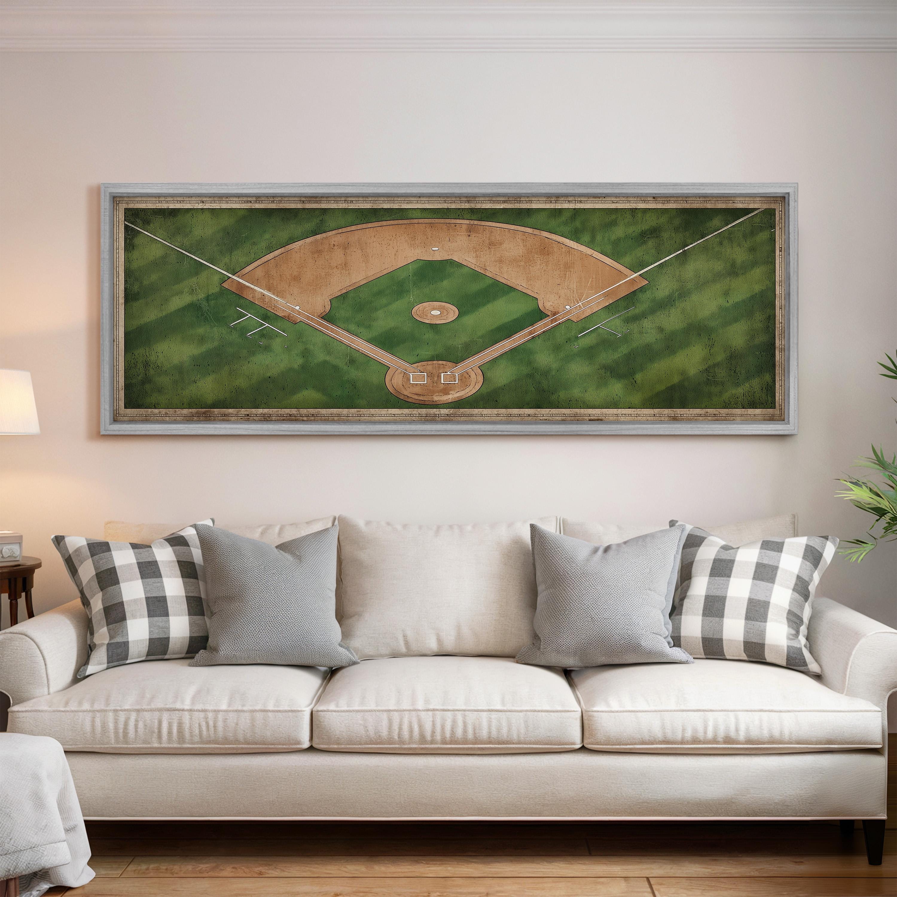 a large framed picture of a baseball field hanging on a wall above a white couch with gray and white pillows.