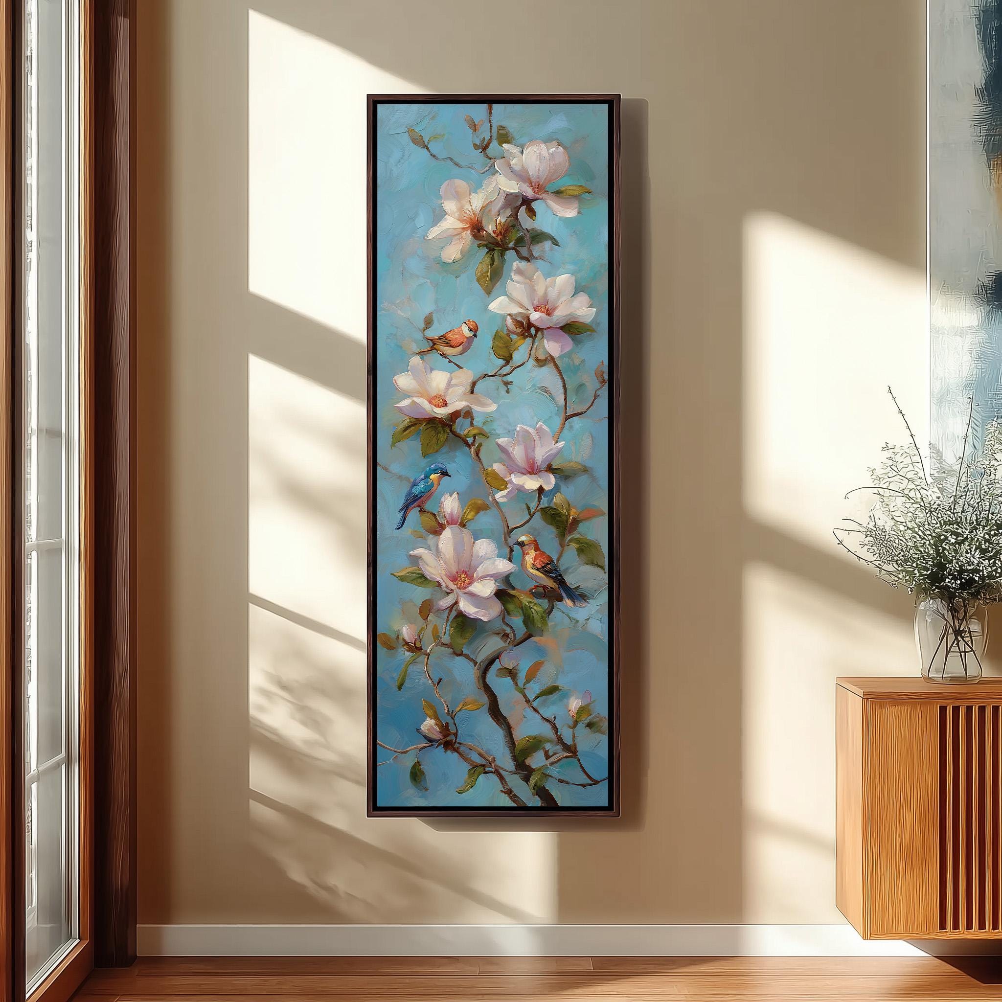 a large painting of pink flowers with green leaves and two birds perched on the branches, hanging on a wall in a room with a wooden cabinet and a vase of flowers.