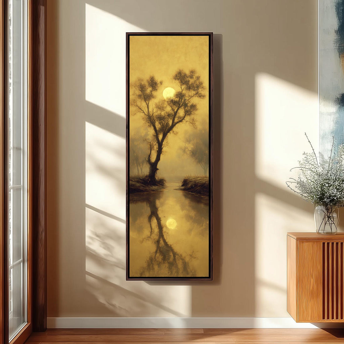 a large framed painting hanging on a wall, depicting a serene landscape with a tree and a body of water reflecting the warm, golden hues of the setting sun.