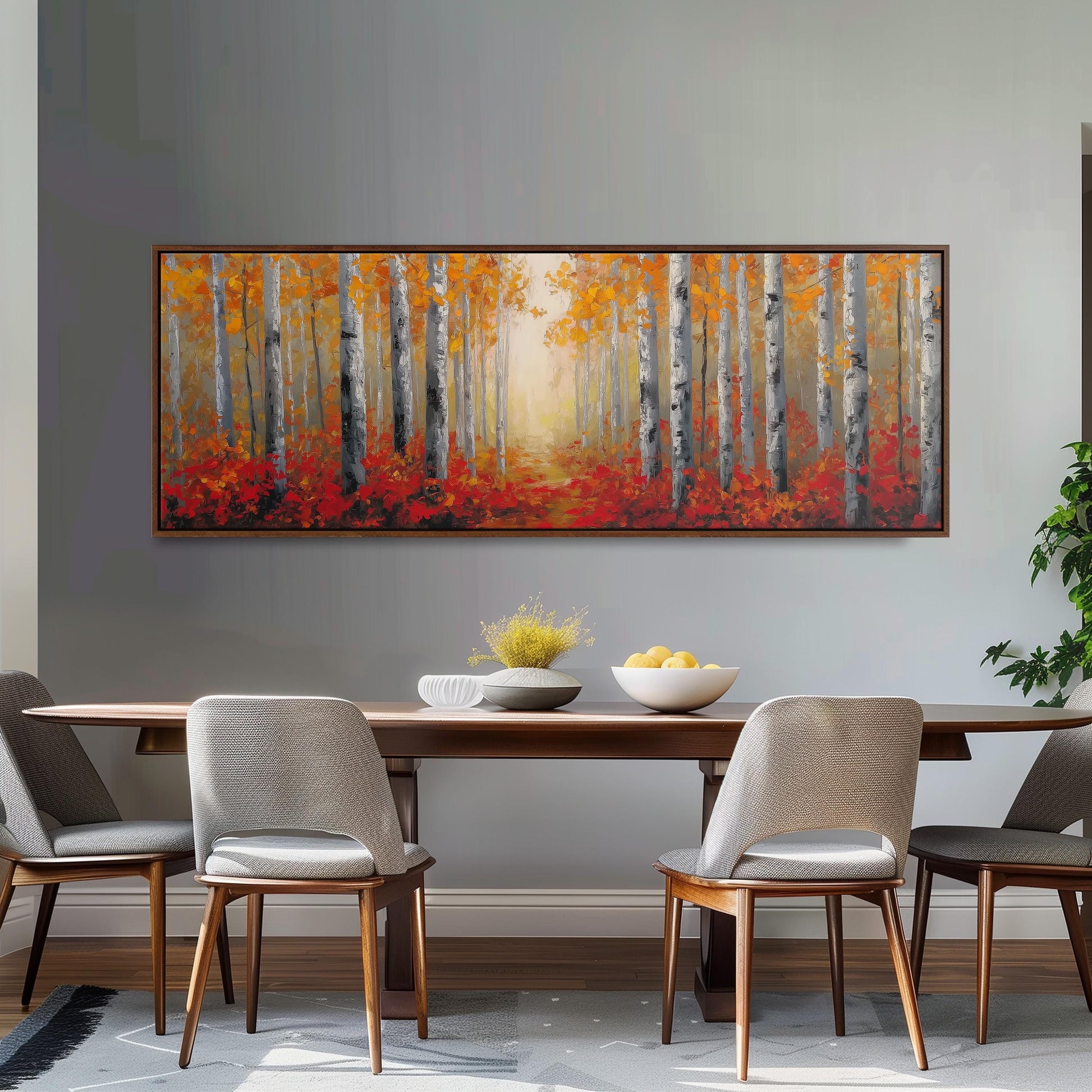 a dining room with a large painting of a forest scene hanging on the wall above a wooden dining table with four chairs. The painting depicts a path leading through a forest of trees with vibrant orange and red foliage.