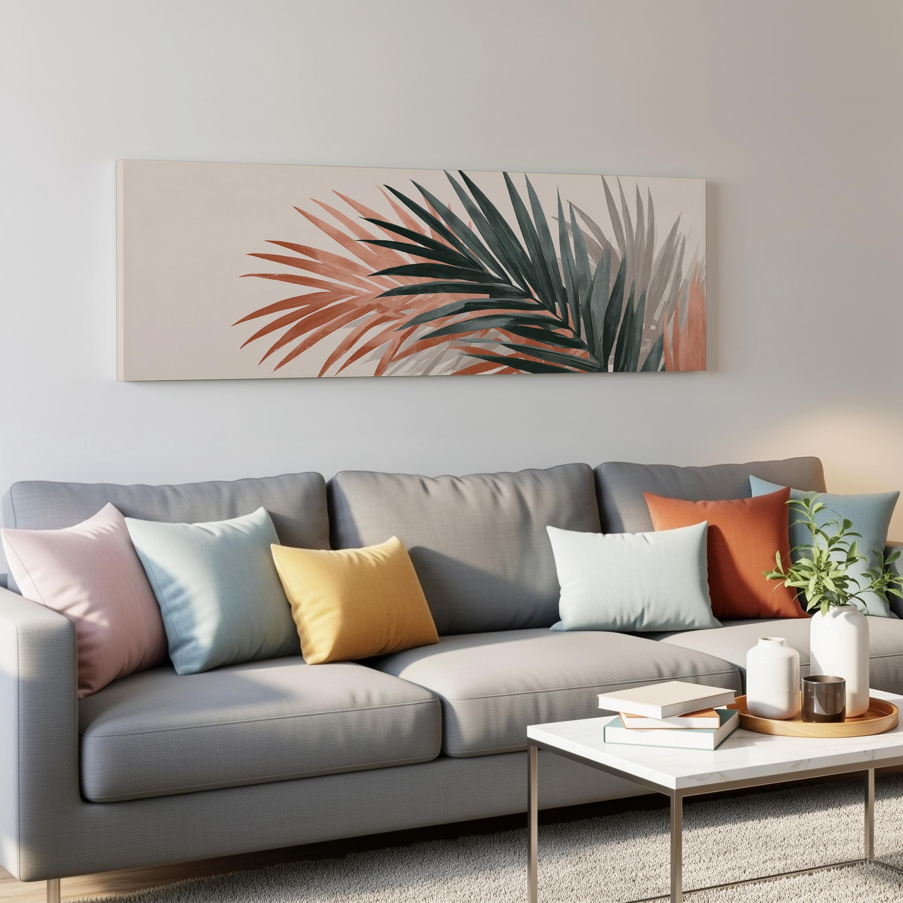 a modern living room with a gray sofa adorned with colorful throw pillows. Above the sofa, there is a large canvas print depicting palm leaves in shades of green, orange, and pink. The room also includes a coffee table with books and a plant, creating a cozy and inviting atmosphere.