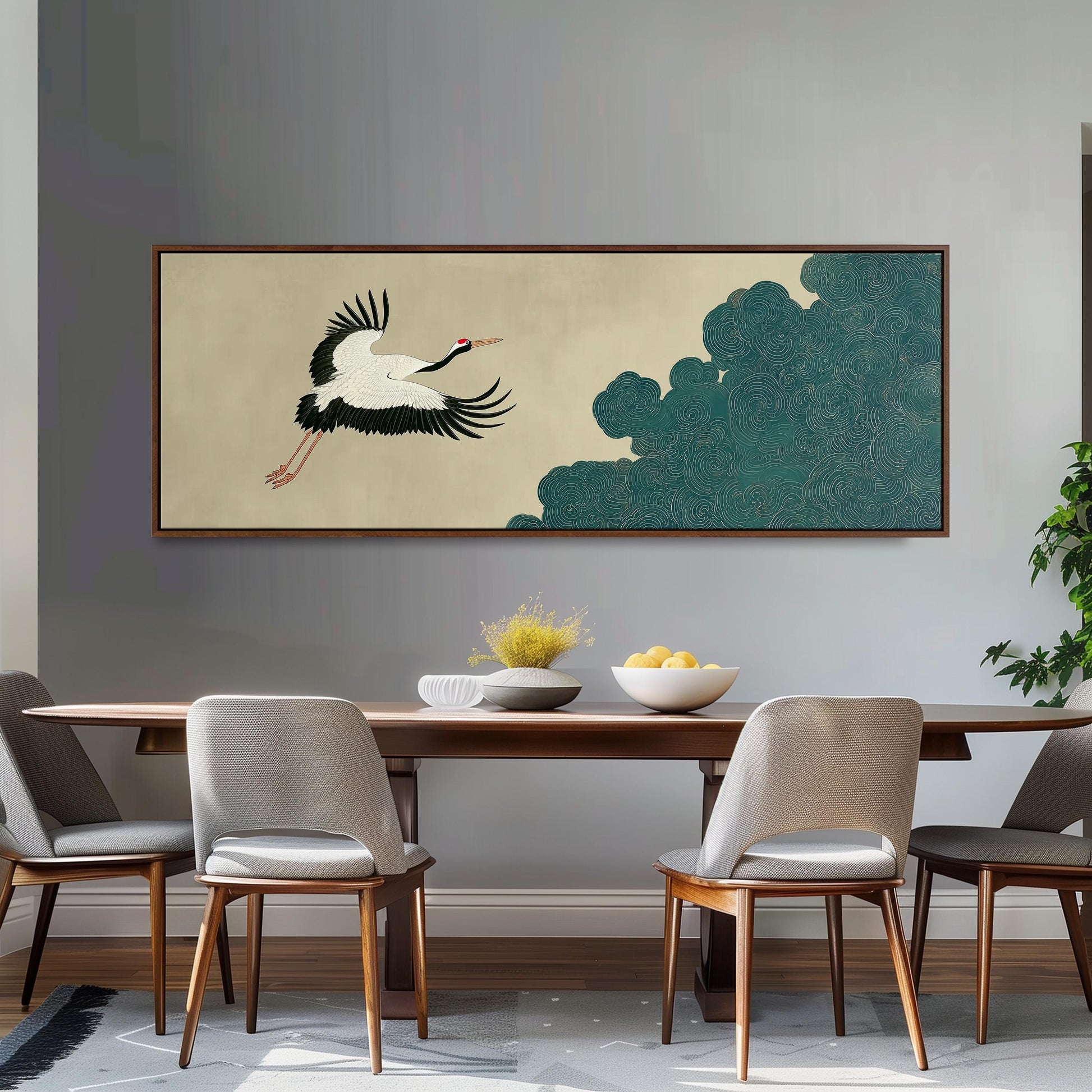 a dining room with a wooden table and four chairs. Above the table, there is a large painting depicting a crane in flight. The painting is framed and hangs on the wall. The table is set with a bowl of fruit and a vase of flowers, creating a welcoming and elegant atmosphere.
