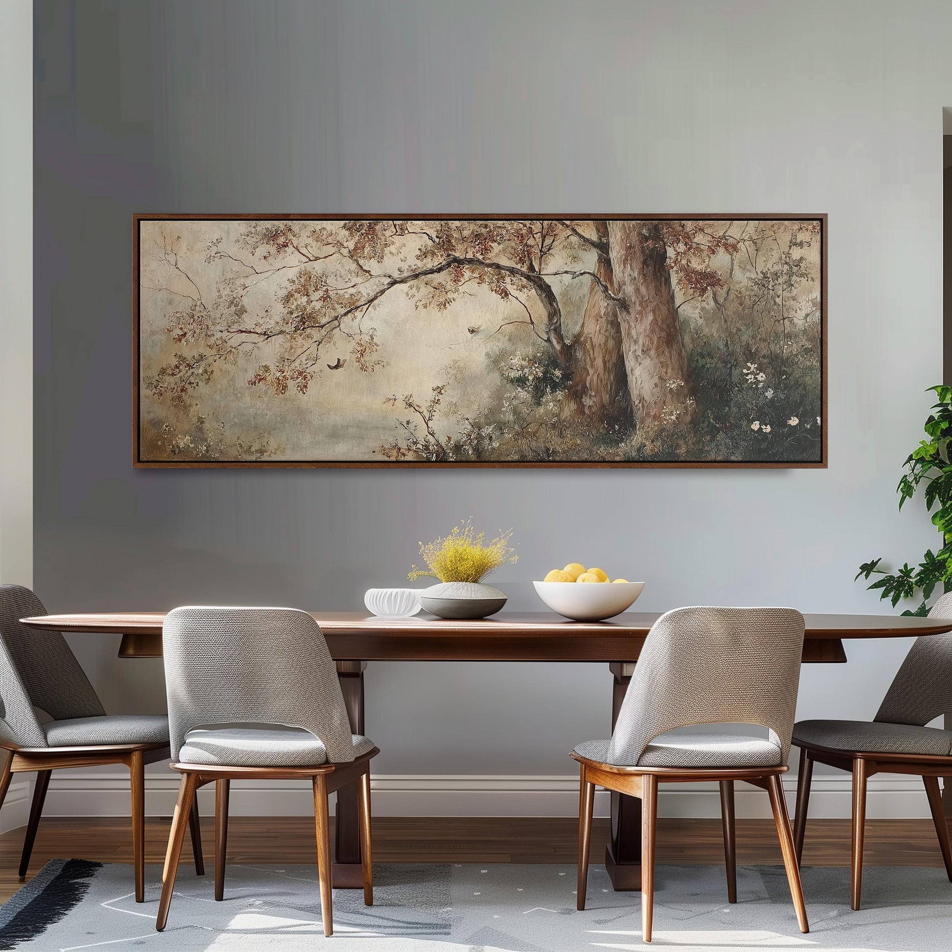 a dining room with a large painting of trees hanging on the wall above a wooden table with four chairs. The table is set with a bowl of fruit and a vase of flowers, creating a cozy and inviting atmosphere.