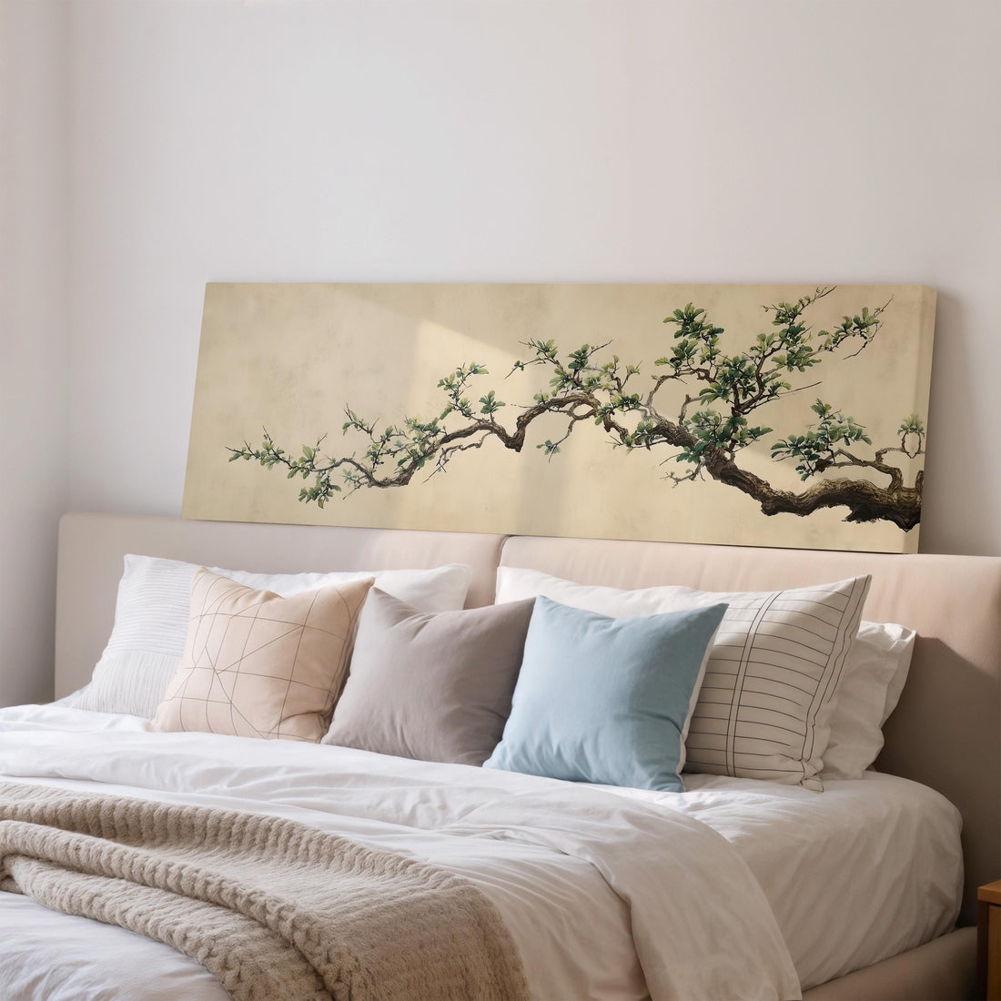 a large, framed painting of a tree branch with green leaves hanging above a brown sofa in a living room setting.