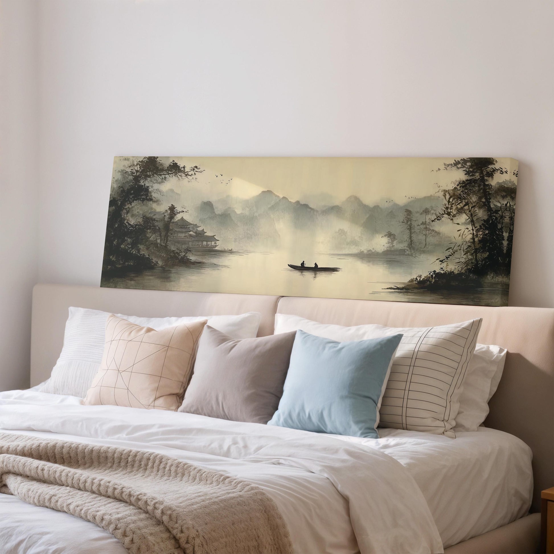 a large painting of a serene landscape with a boat on a lake, hanging above a bed with white pillows and a gray blanket.