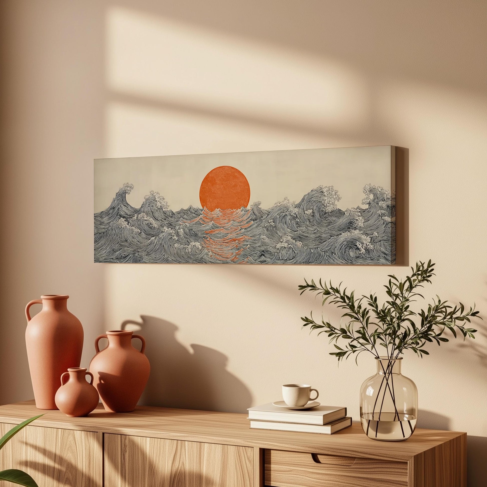 a wooden cabinet with a vase, a plant, and a stack of books on top. Above the cabinet, there is a painting depicting a sunset over the ocean with waves crashing against the shore.
