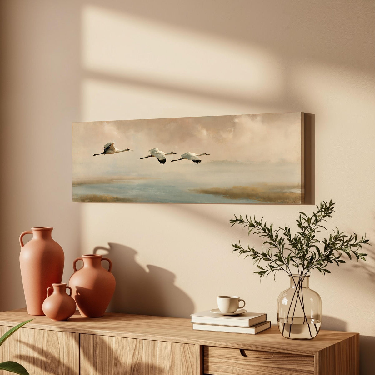 Cranes flying over a calm shore at dusk long horizontal canvas print above a wooden sideboard