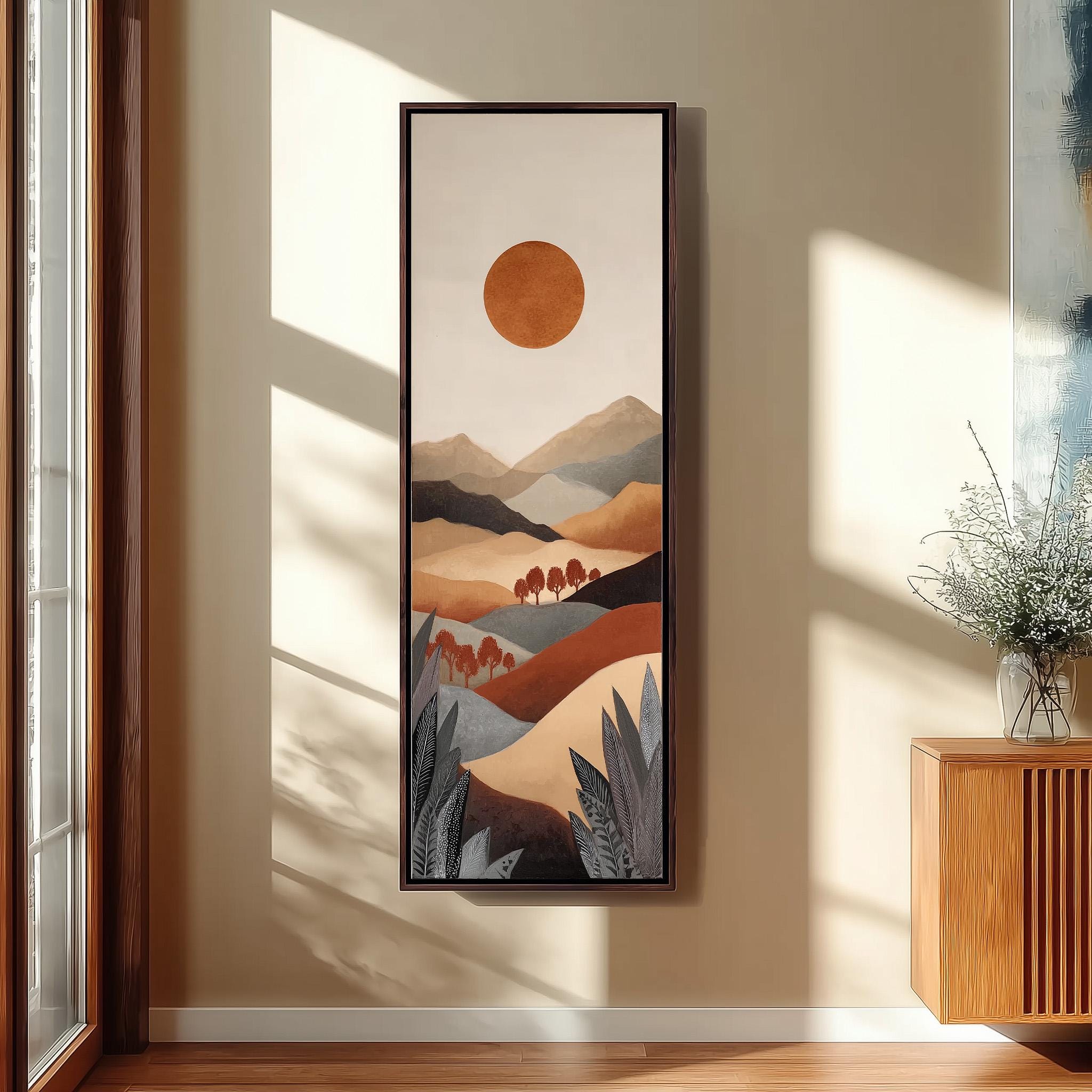 a large framed painting hanging on a wall, depicting a landscape with mountains, trees, and a large orange circle in the sky.