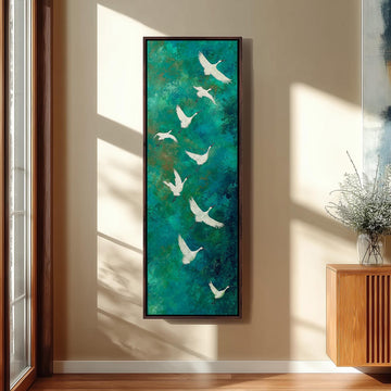 a large painting of white birds flying against a green background, hanging on a wall in a room with a wooden cabinet and a vase of flowers.