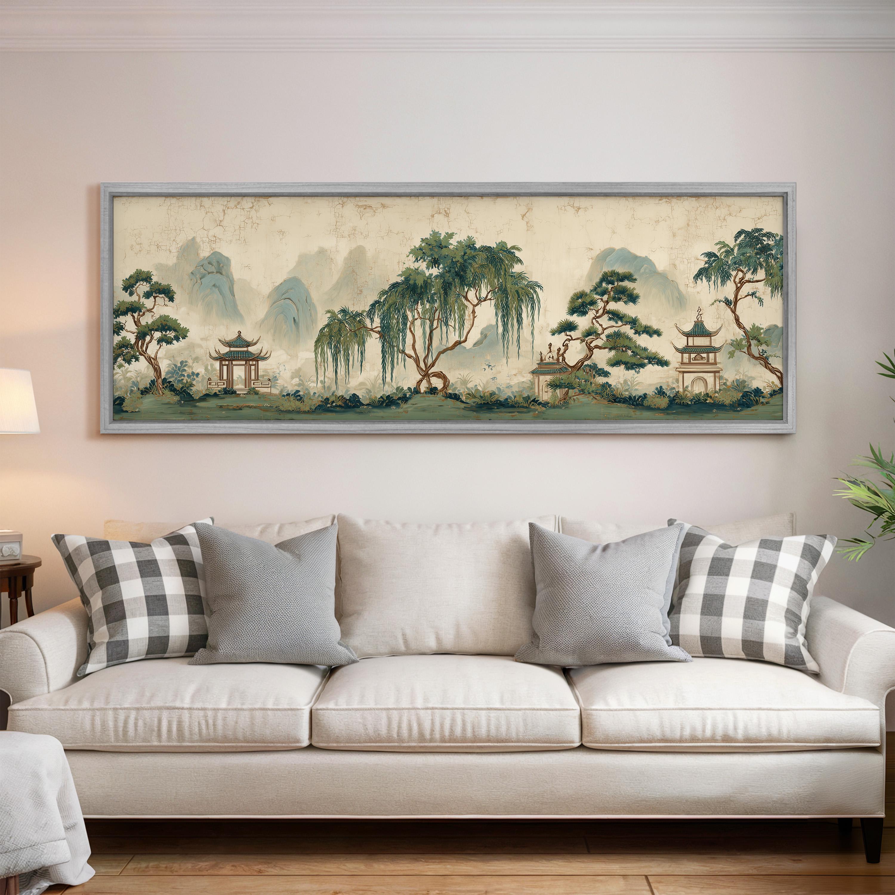 a large, framed painting of a serene landscape with mountains, trees, and pagodas hanging on a wall above a white sofa with gray and white patterned pillows.