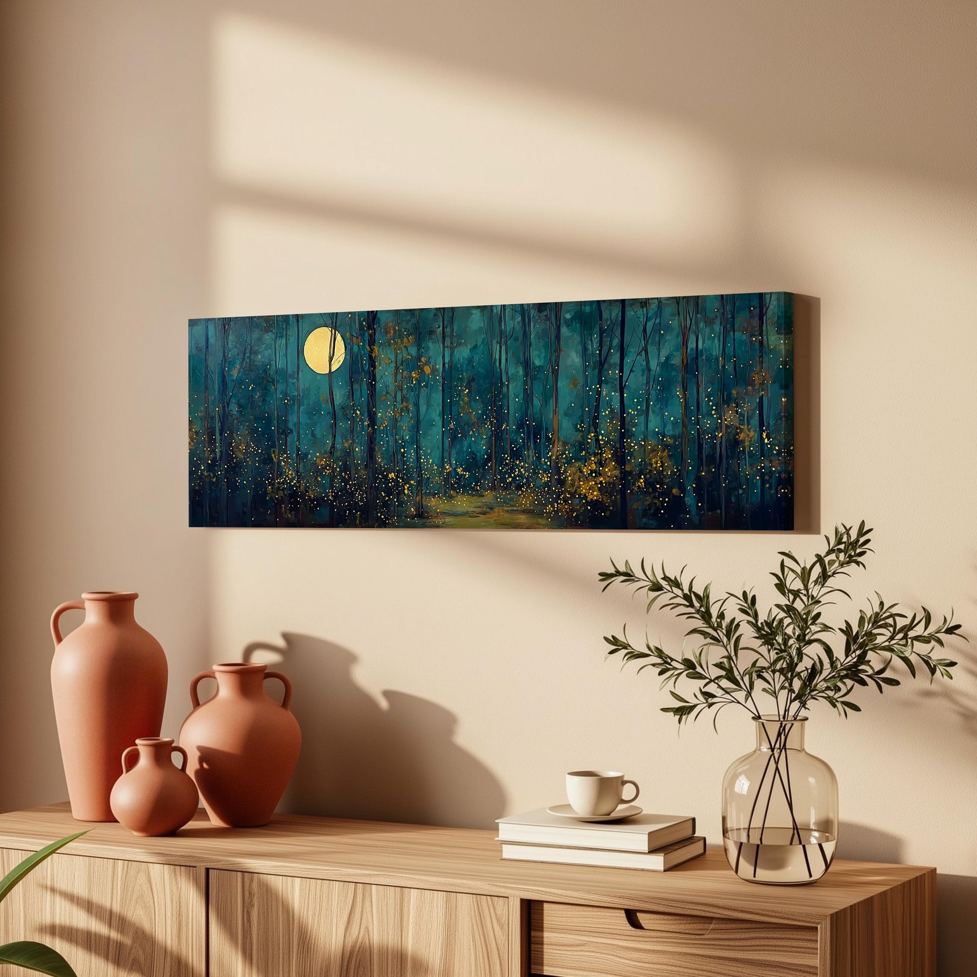 a wooden cabinet with a painting of a forest scene hanging on the wall above it. The painting depicts a serene night scene with a full moon illuminating the trees. The cabinet also has three orange vases, a white coffee cup, and a stack of books on top.
