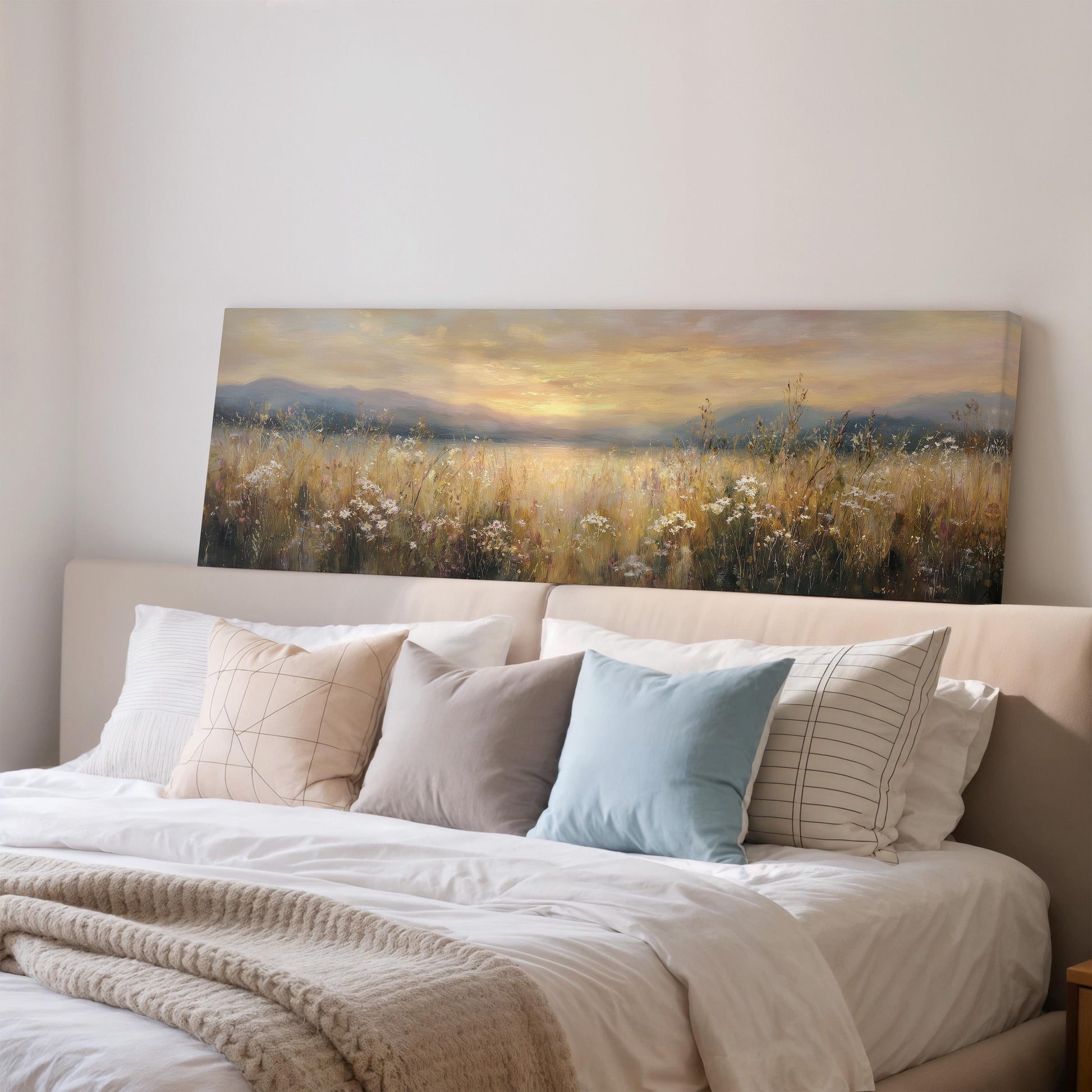 a large painting of a field with a sunset in the background, hanging above a bed with white pillows and a gray blanket.