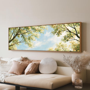 Sunlit leafy branches framing soft clouds long horizontal canvas print above a sofa in a living room