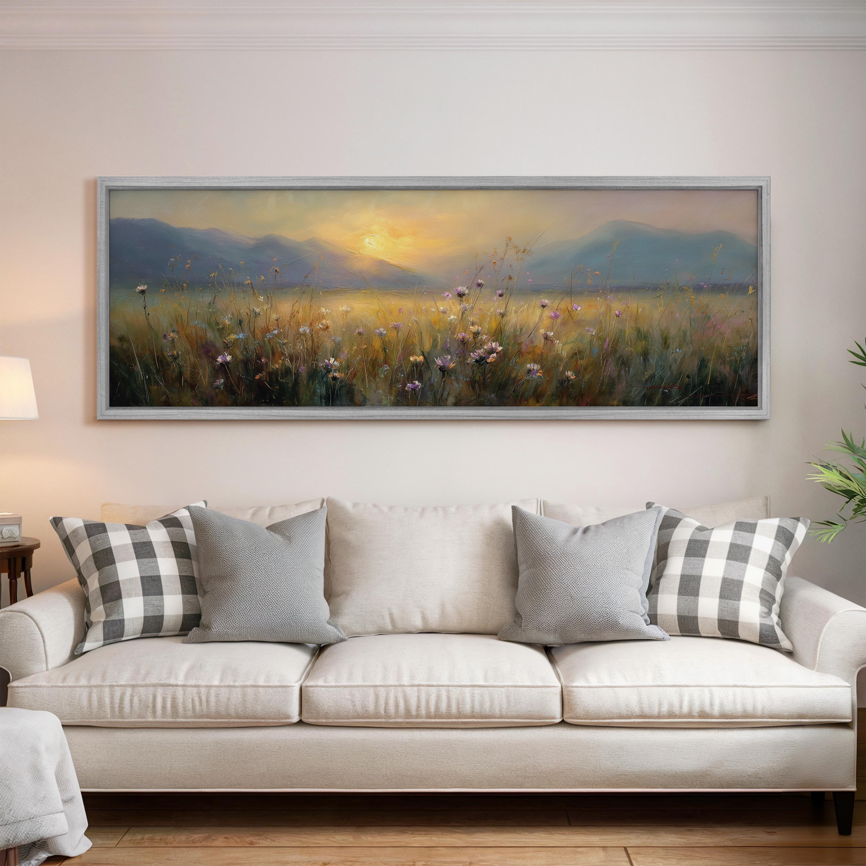 a large painting of a field with flowers hanging on the wall above a white sofa with gray and white pillows.