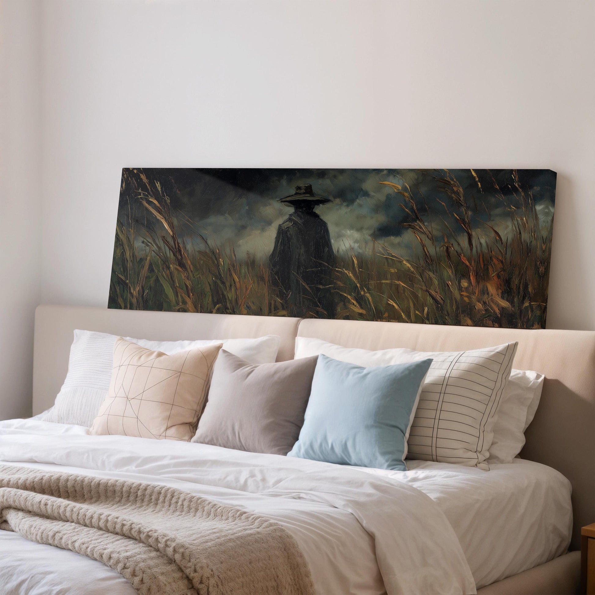 a large painting of a person in a field of tall grass, hanging on a wall above a bed with white pillows and a gray blanket.