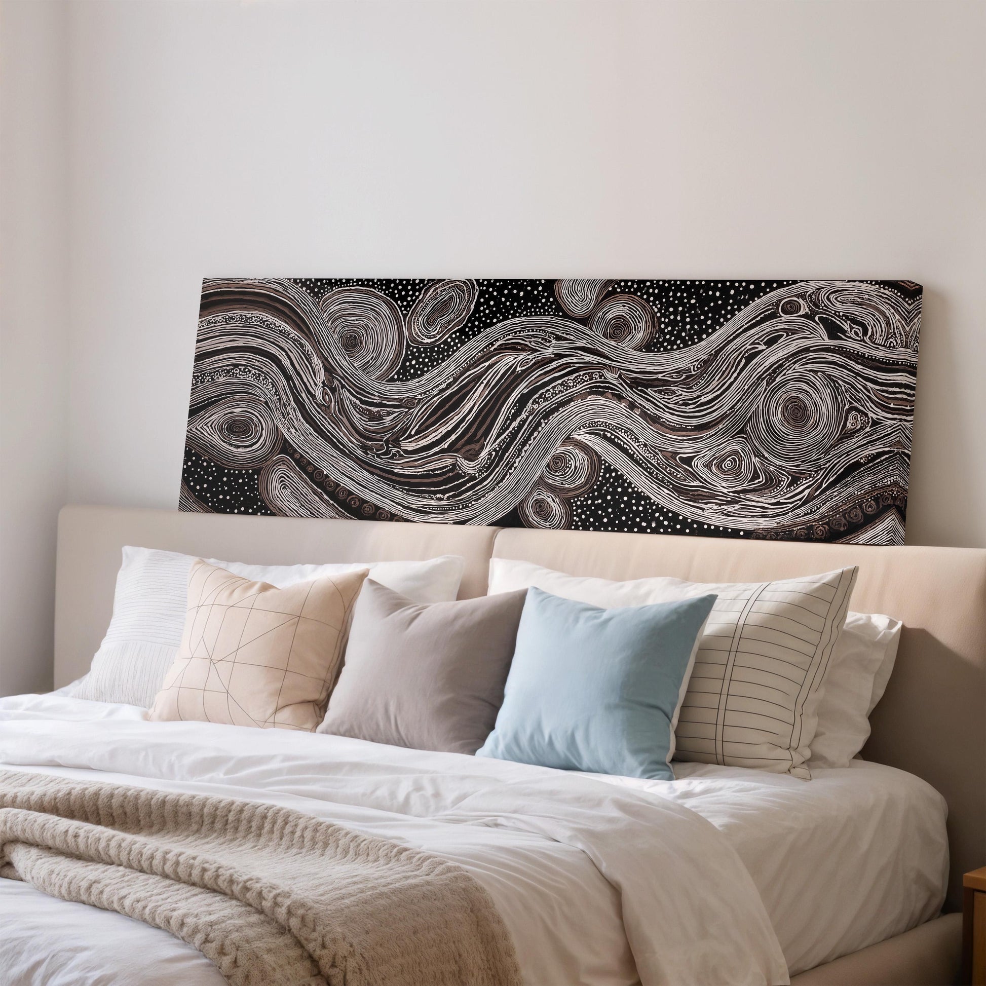 a cozy bedroom with a large bed adorned with white linens and a variety of colorful pillows. Above the bed, there is a striking black and white abstract artwork featuring swirling patterns and shapes.