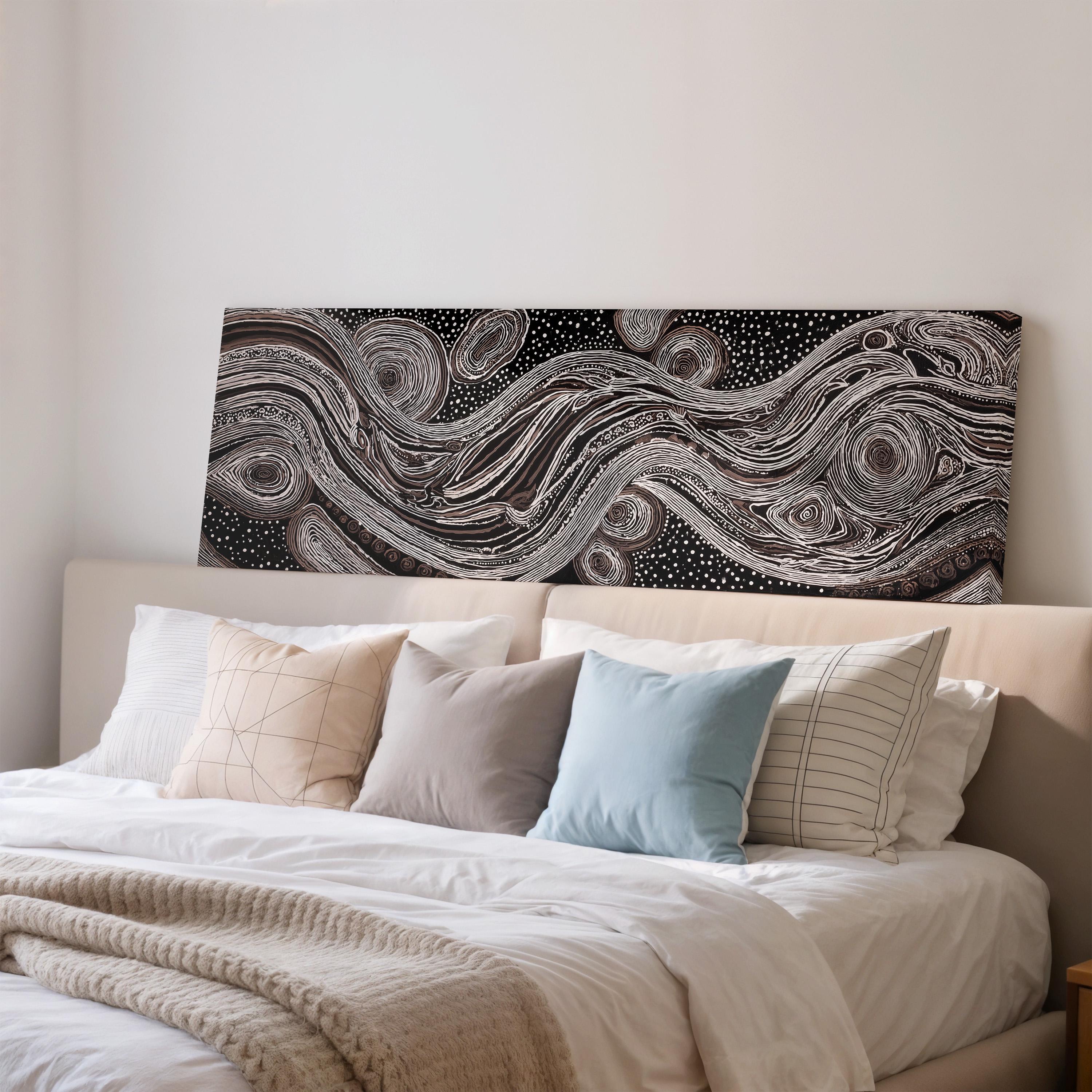 a cozy bedroom with a large bed adorned with white linens and a variety of colorful pillows. Above the bed, there is a striking black and white abstract artwork featuring swirling patterns and shapes.