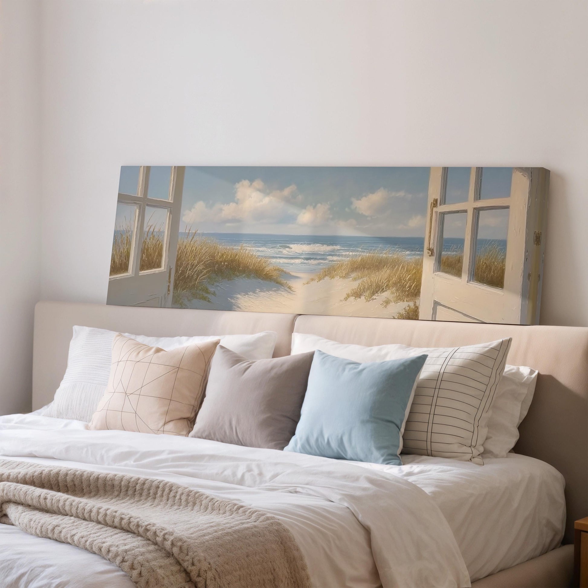 a large bedroom with a bed and a painting of a beach scene above it. The bed has white sheets and pillows, and the painting depicts a beach with a path leading to the ocean.