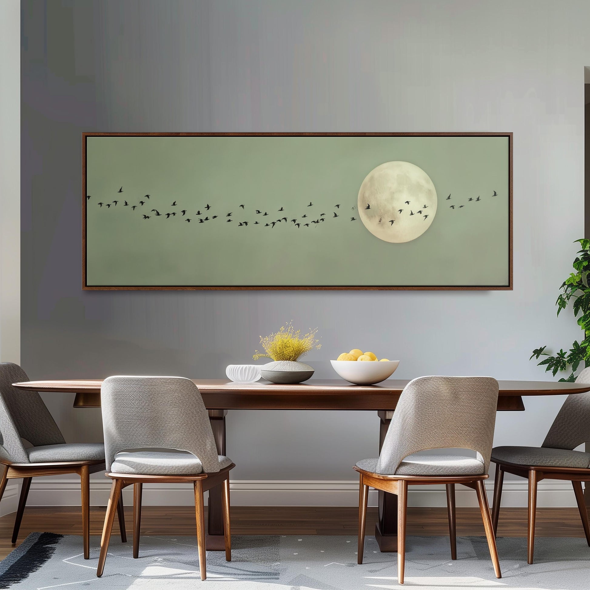 a dining room with a large framed picture of a flock of birds flying over a moon on the wall above a wooden dining table with four chairs.
