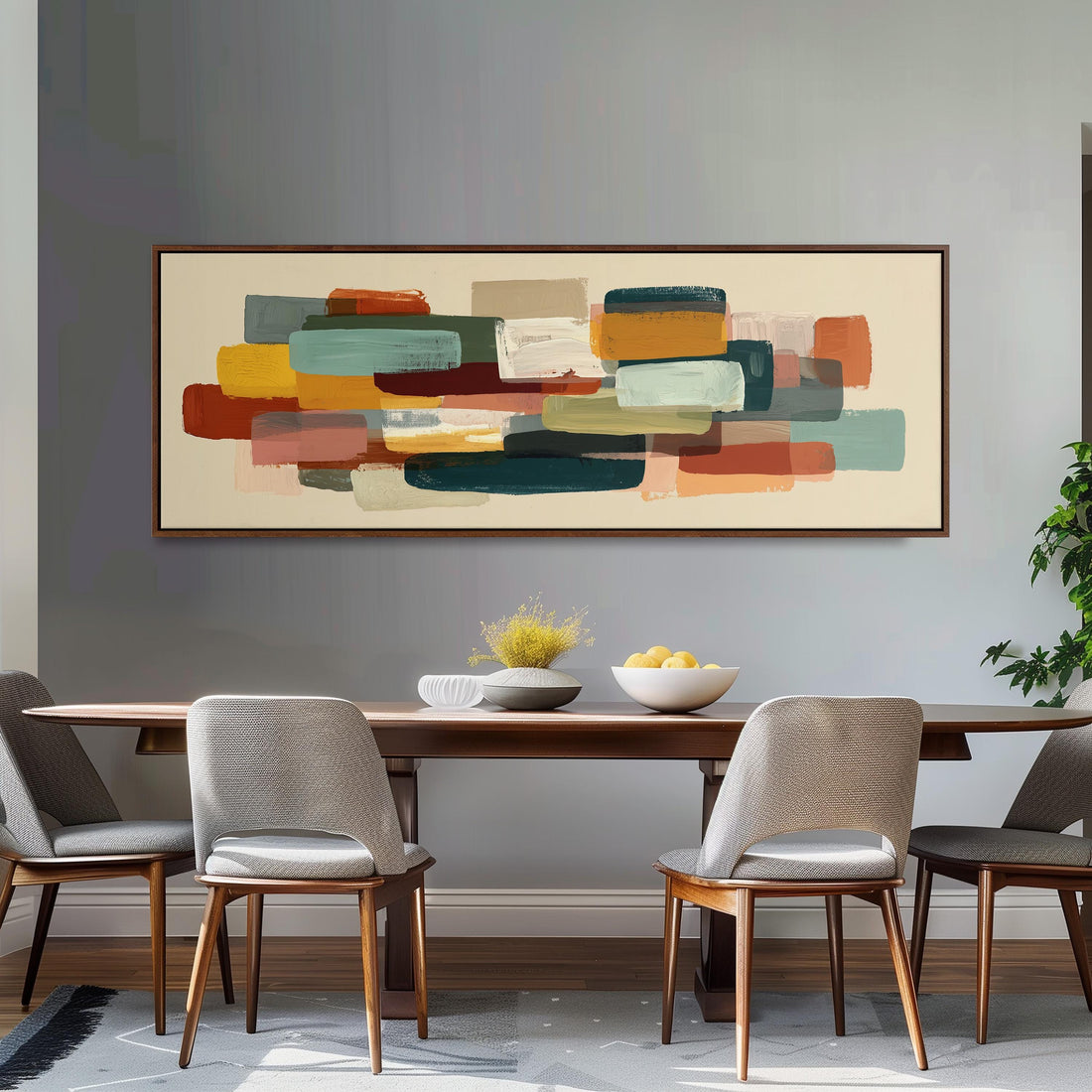 a dining room with a wooden table and four chairs. Above the table, there is a large abstract painting with various colors and shapes. The table is set with a bowl of fruit and a vase of flowers, creating a cozy and inviting atmosphere.