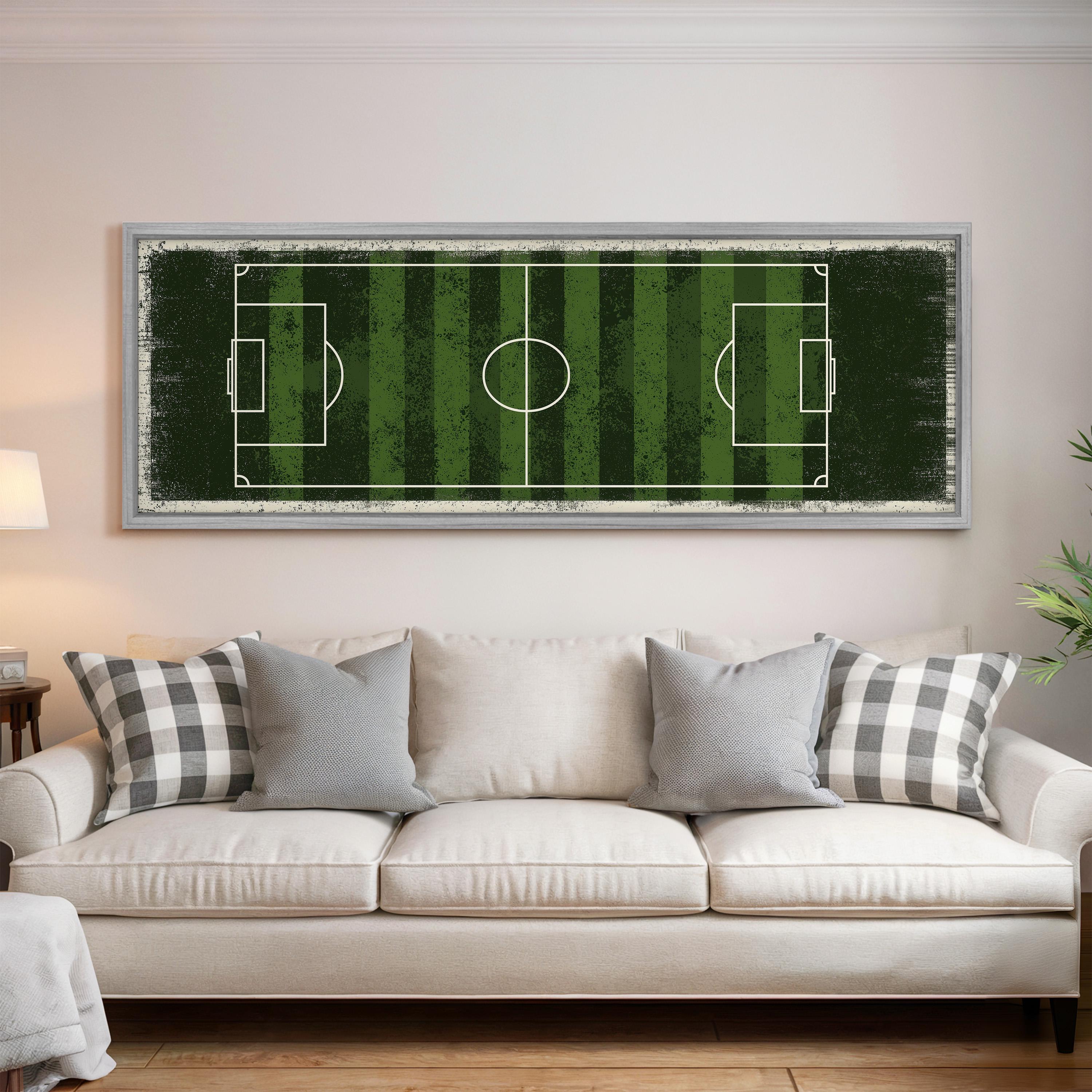 a large framed picture of a soccer field hanging on a wall above a white couch in a living room.