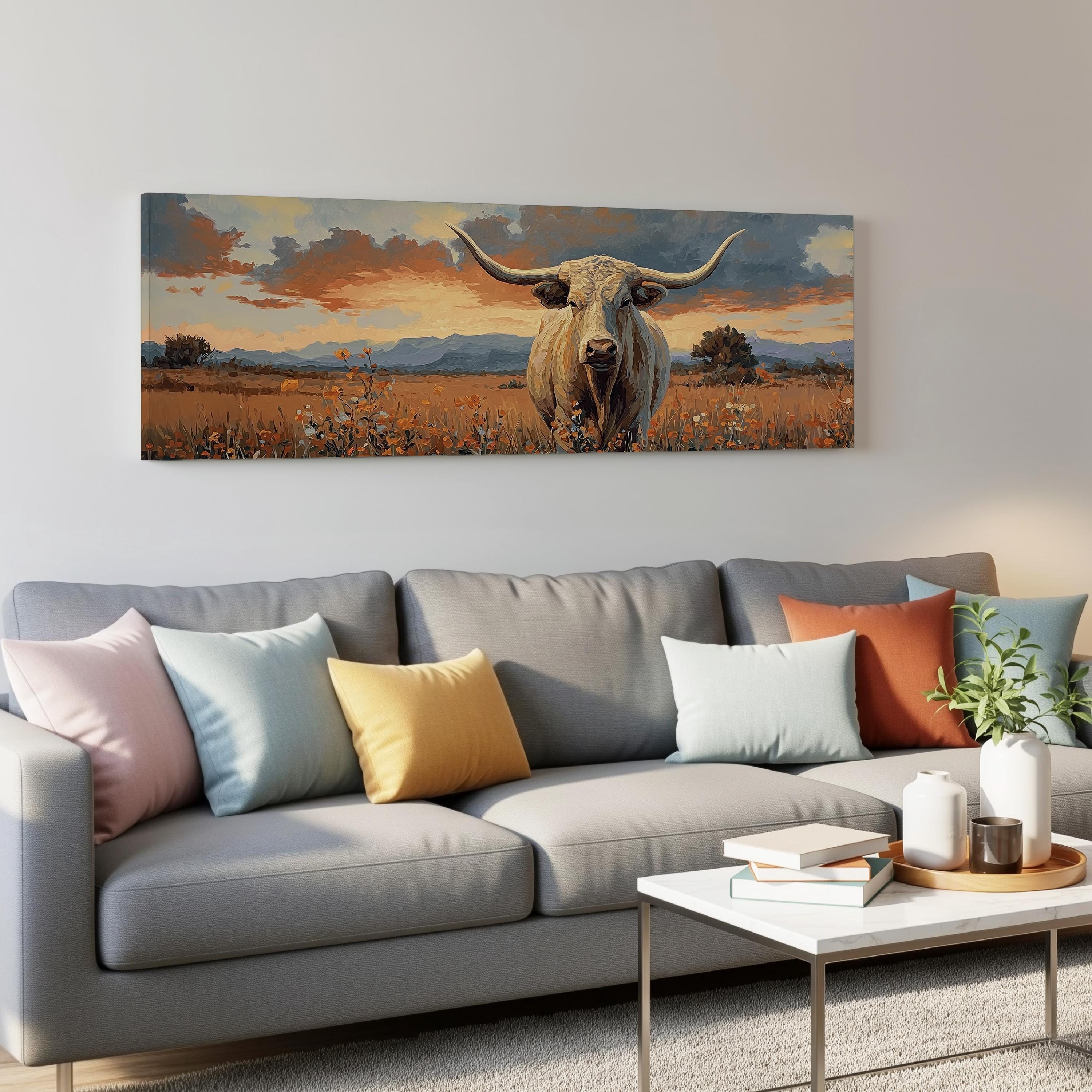 a large painting of a bull with long horns hanging on a wall above a gray couch with colorful throw pillows.
