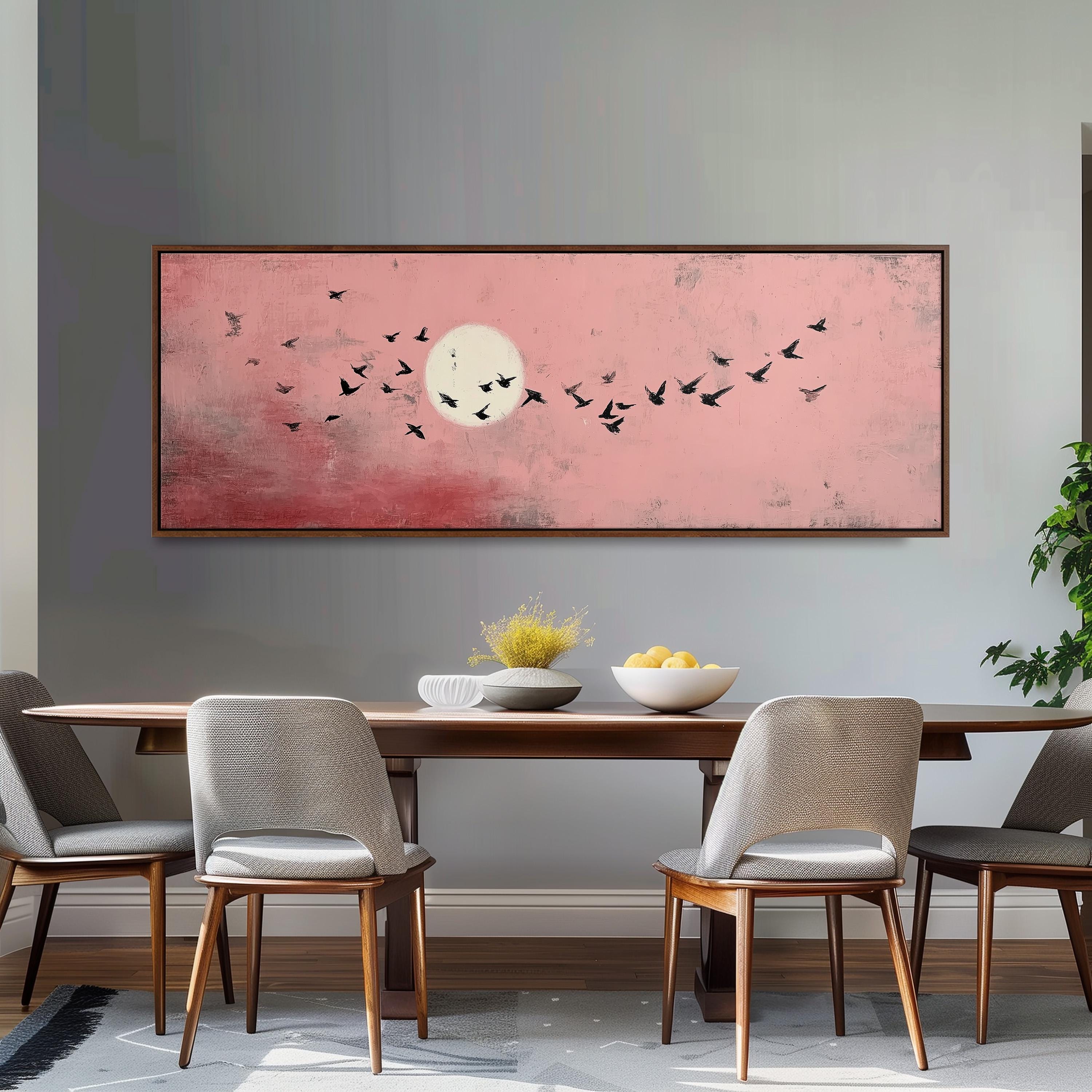 a dining room with a large painting of a flock of birds against a pink and red sky hanging on the wall above a wooden dining table with four chairs.