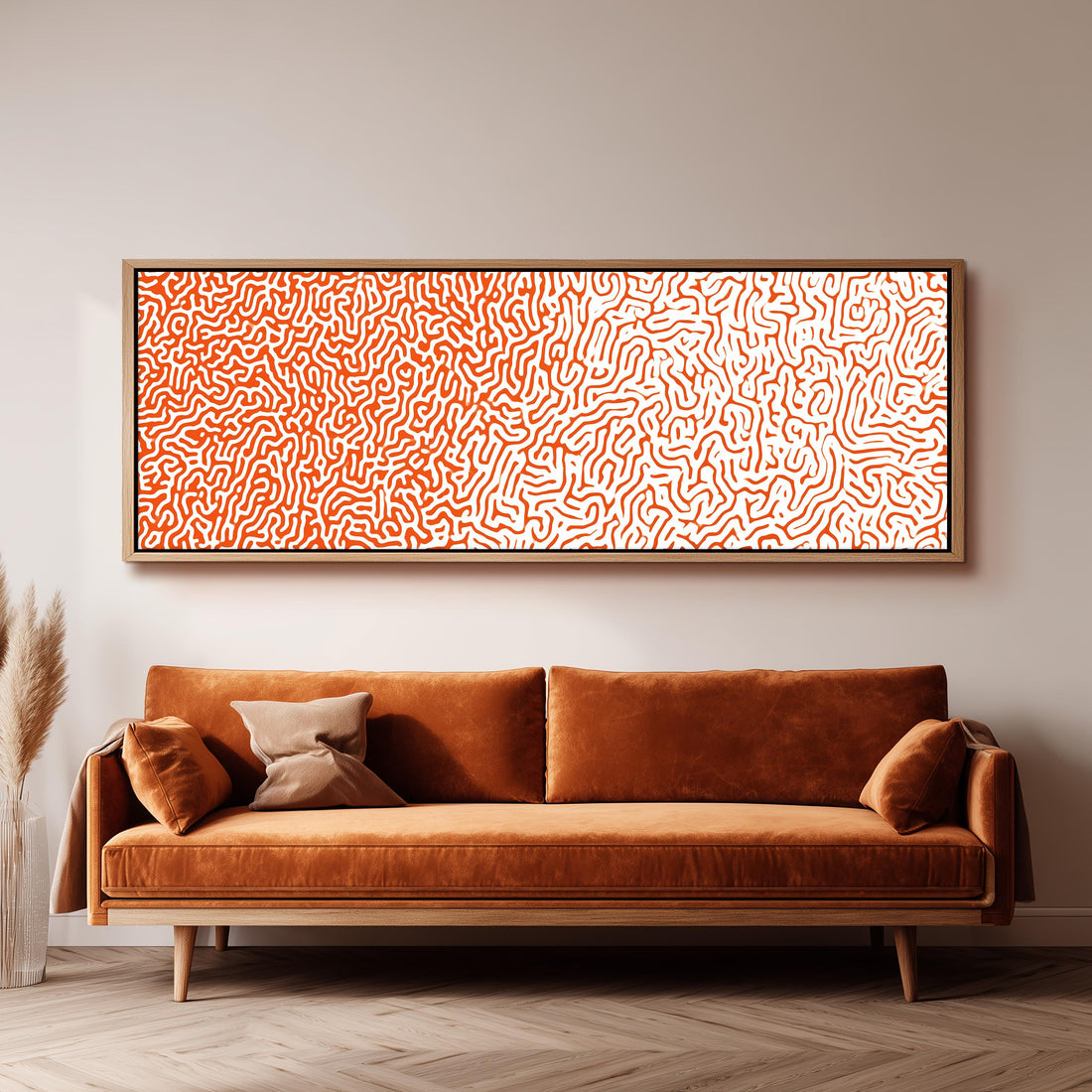 a large, rectangular, orange-colored couch with a brown pillow on it, positioned in front of a white wall. Above the couch, there is a framed artwork with a pattern of orange and white swirls.