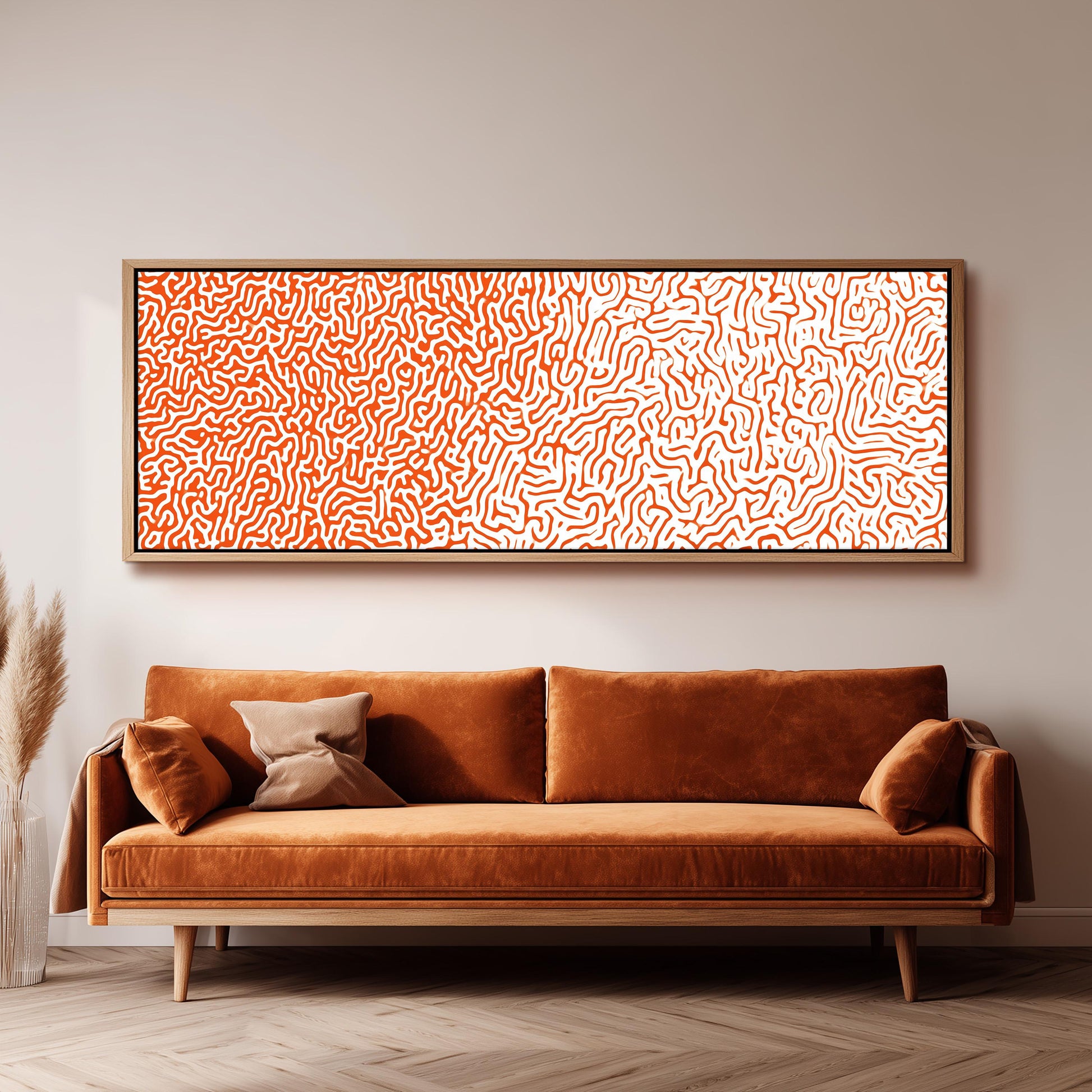 a large, rectangular, orange-colored couch with a brown pillow on it, positioned in front of a white wall. Above the couch, there is a framed artwork with a pattern of orange and white swirls.