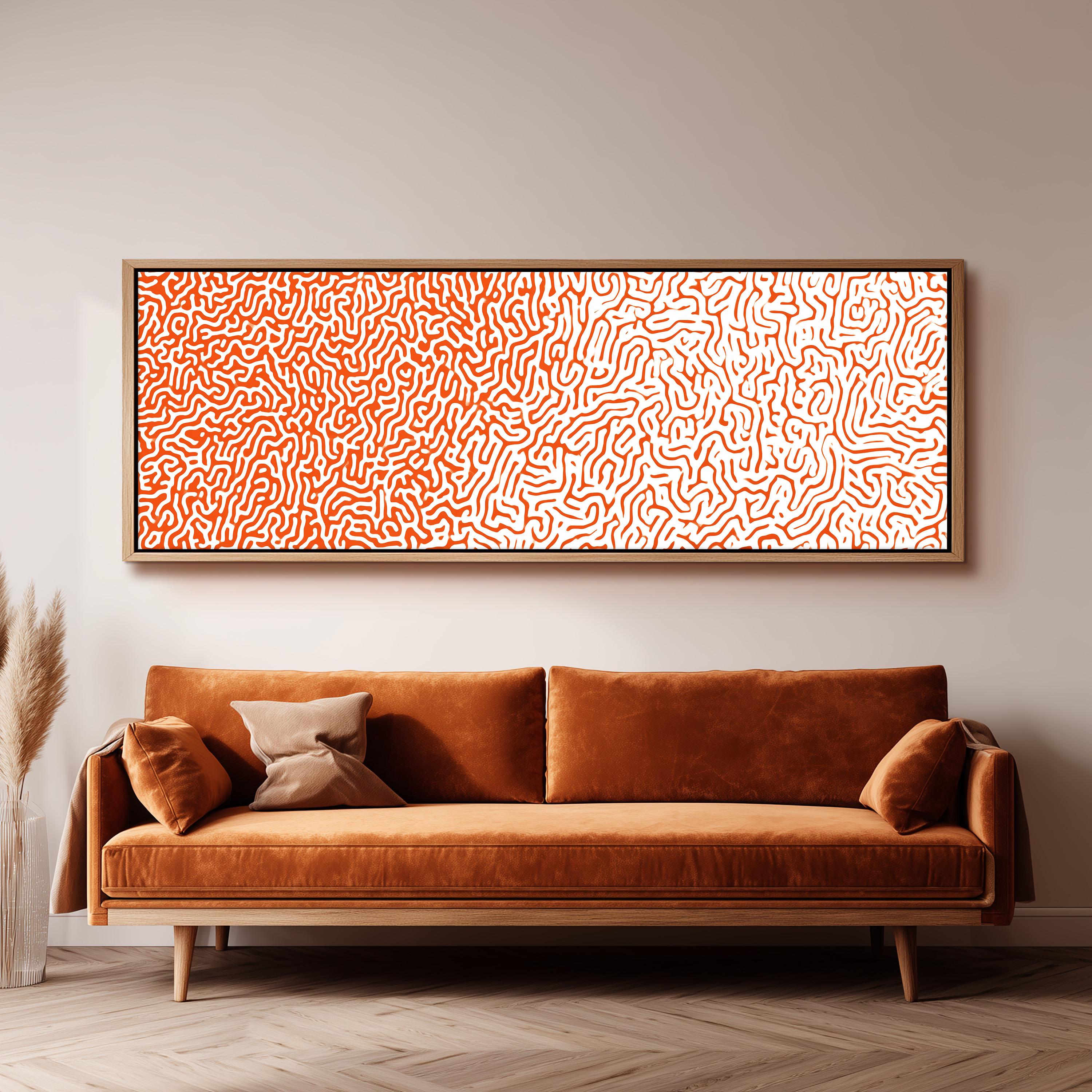 a large, rectangular, orange-colored couch with a brown pillow on it, positioned in front of a white wall. Above the couch, there is a framed artwork with a pattern of orange and white swirls.