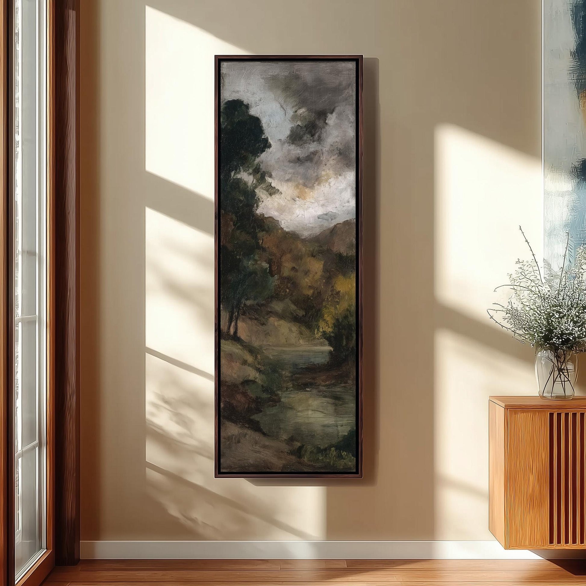 a large landscape painting hanging on a wall, with a wooden cabinet and a vase of flowers to the right of the painting.