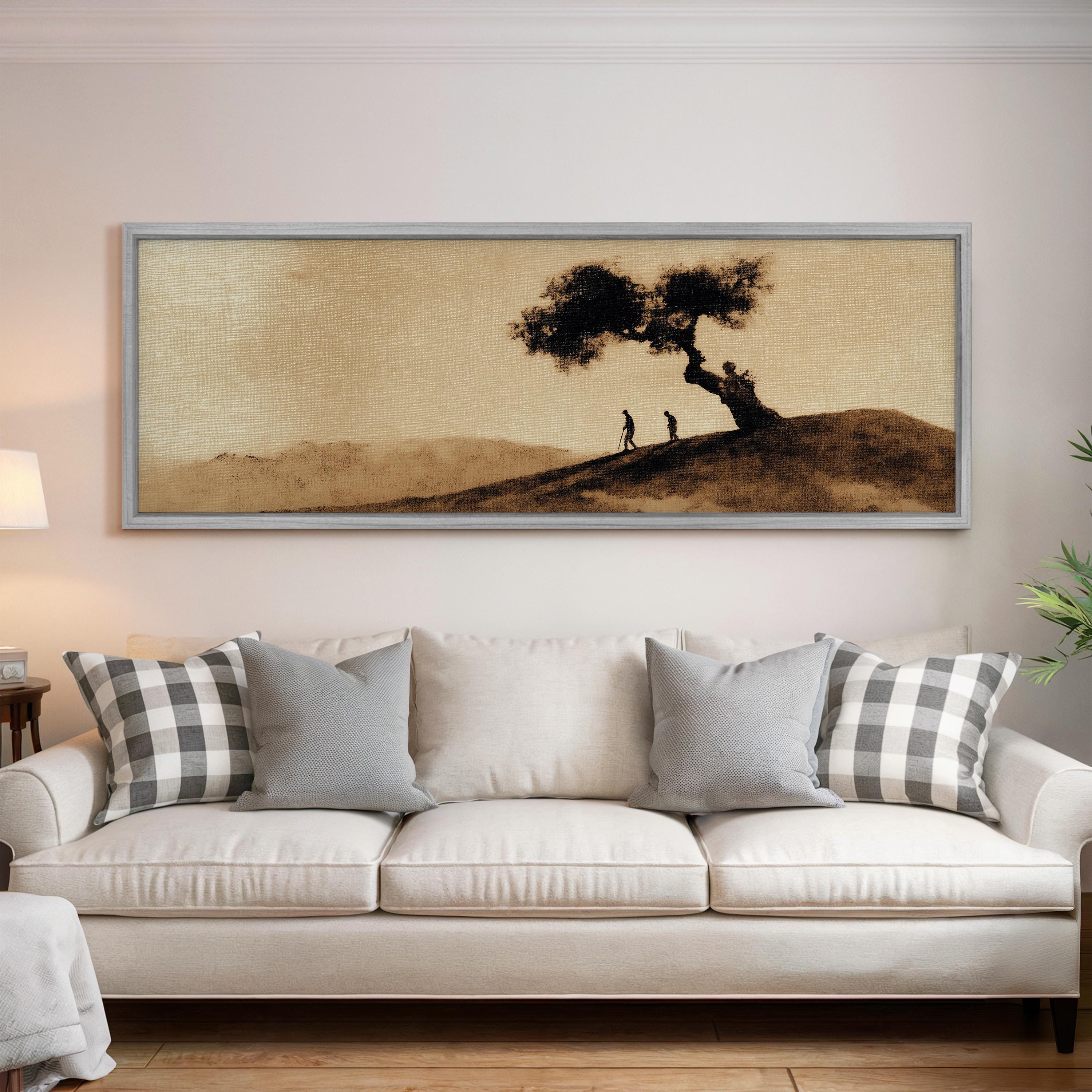 a large framed painting of a tree and two people on a hill, hanging on a wall above a white couch with gray and white plaid throw pillows.