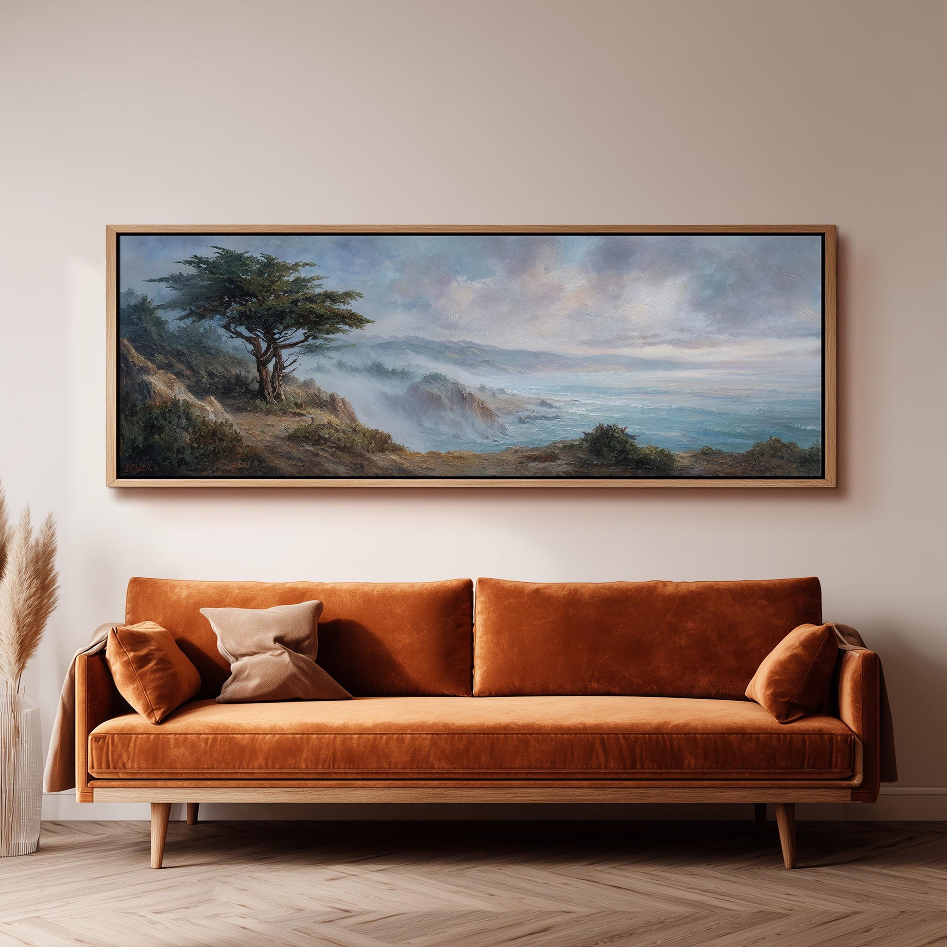 a large painting of a landscape hanging on a wall above a brown sofa with orange cushions.
