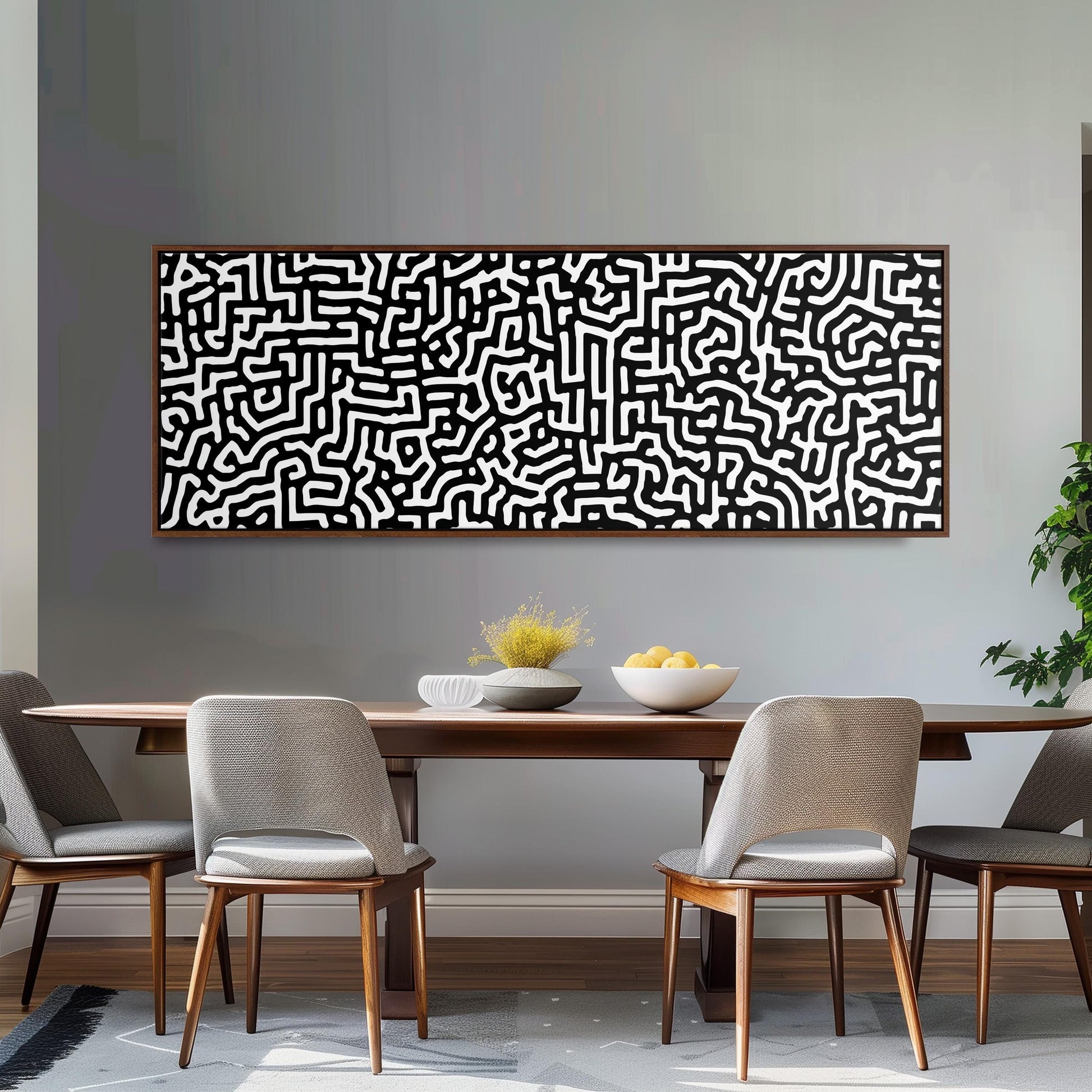 a modern dining room with a wooden table and four chairs. Above the table, there is a large abstract painting with a black and white pattern. On the table, there is a bowl of fruit and a vase of flowers.
