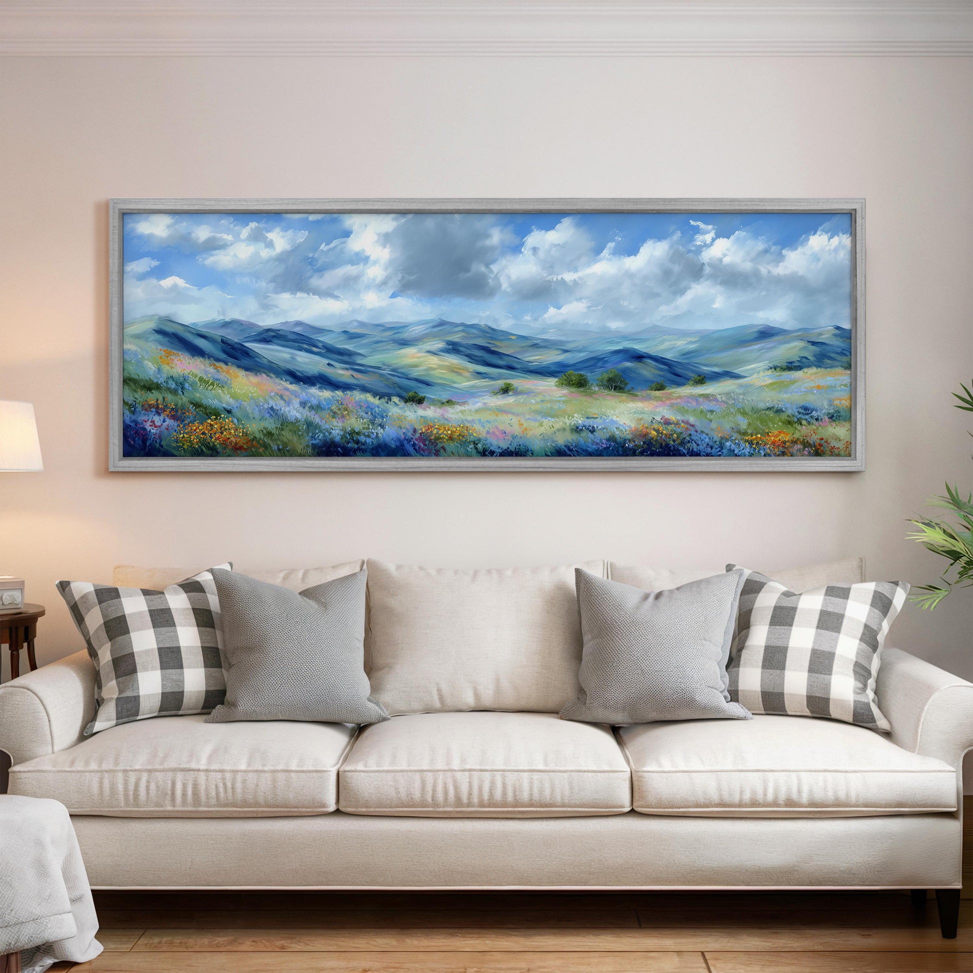 a large, framed painting of a scenic landscape hanging on a wall above a white sofa with gray and white patterned pillows.