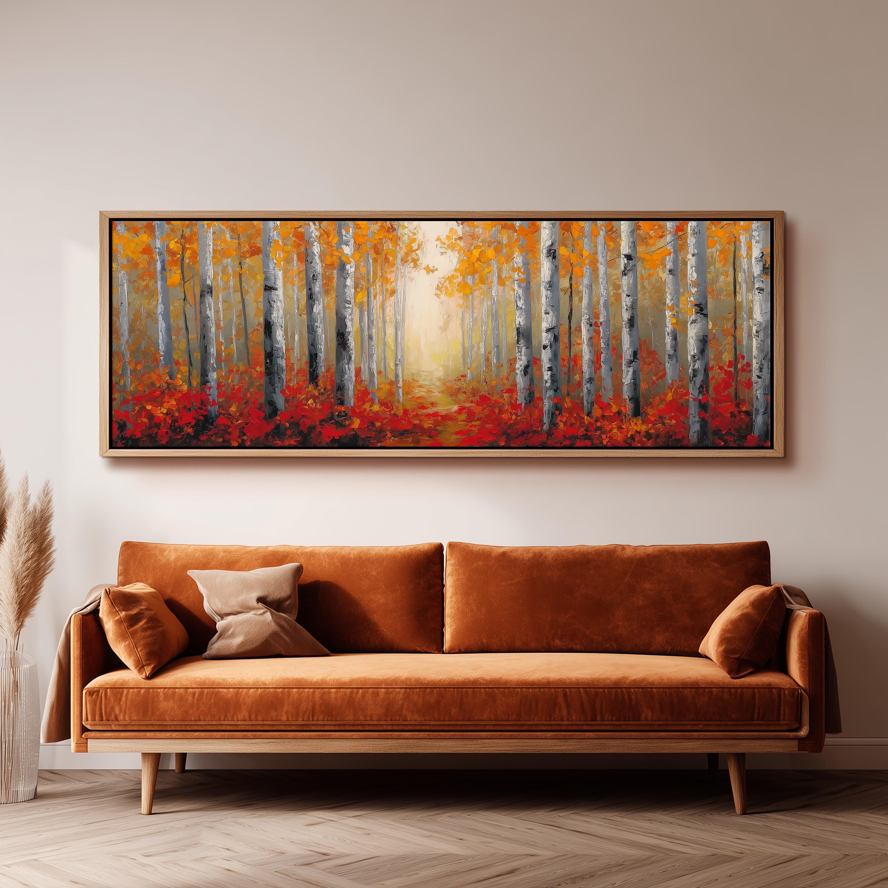 a large, rectangular painting of a forest scene with tall trees and vibrant orange and red foliage. The painting is hung on a wall above a brown sofa, creating a cozy and inviting atmosphere in the room.