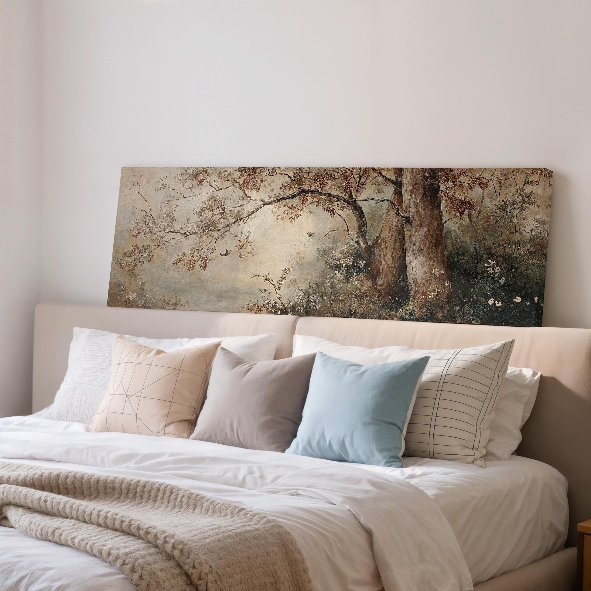 a cozy bedroom with a large bed adorned with white linens and a variety of colorful pillows. Above the bed, there is a painting depicting a serene landscape with trees and a river.