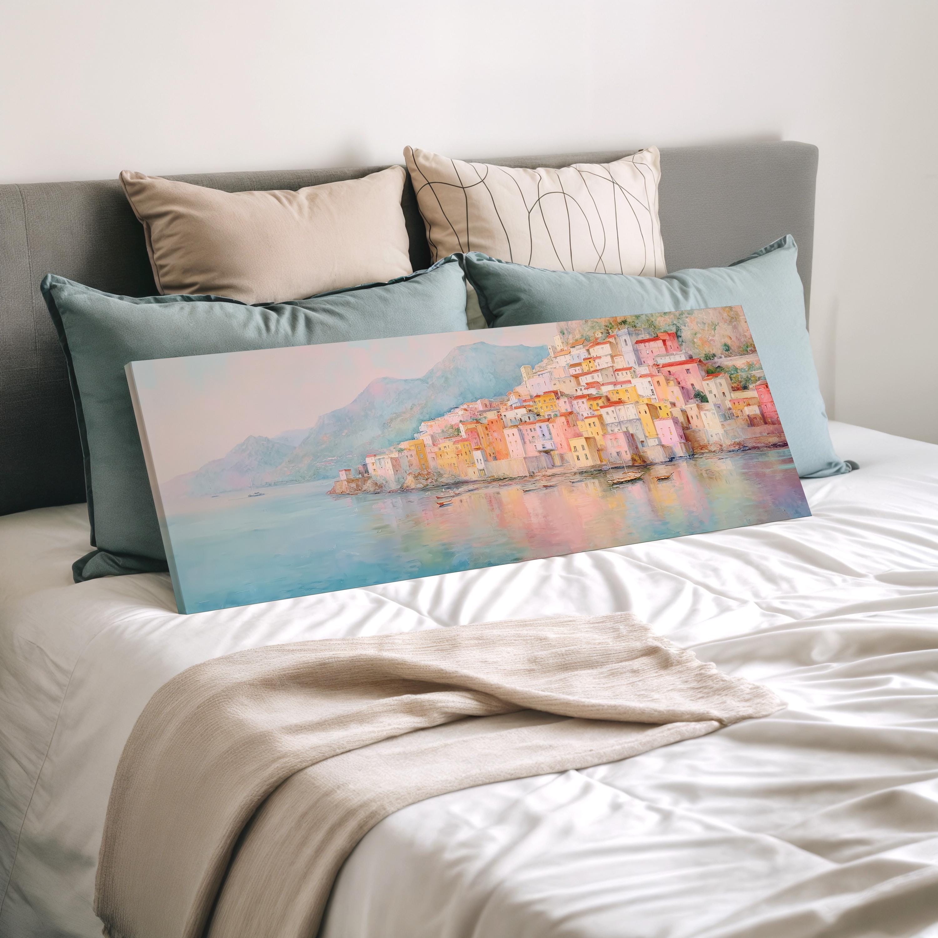 a large painting of a coastal town with colorful buildings and a body of water in the background, displayed on a bed with pillows.