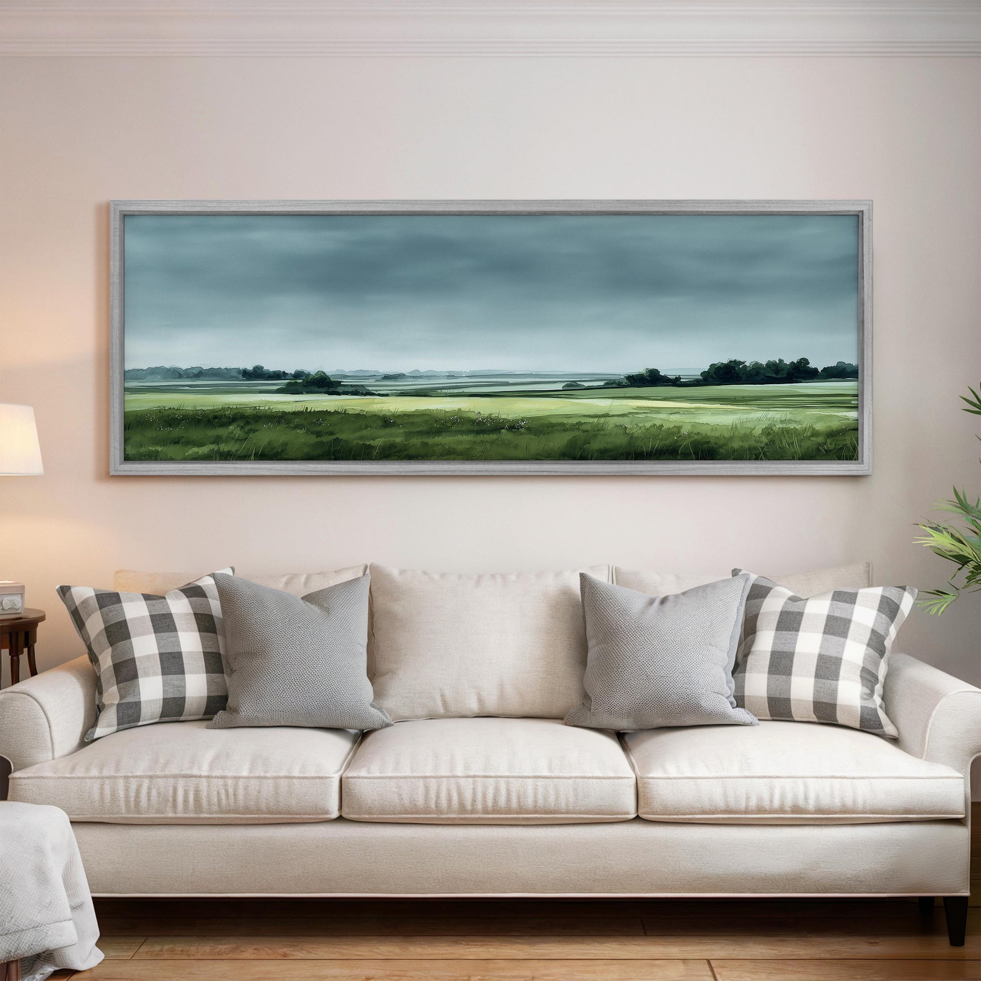 a large landscape painting hanging on a wall above a white sofa with gray and white patterned pillows.