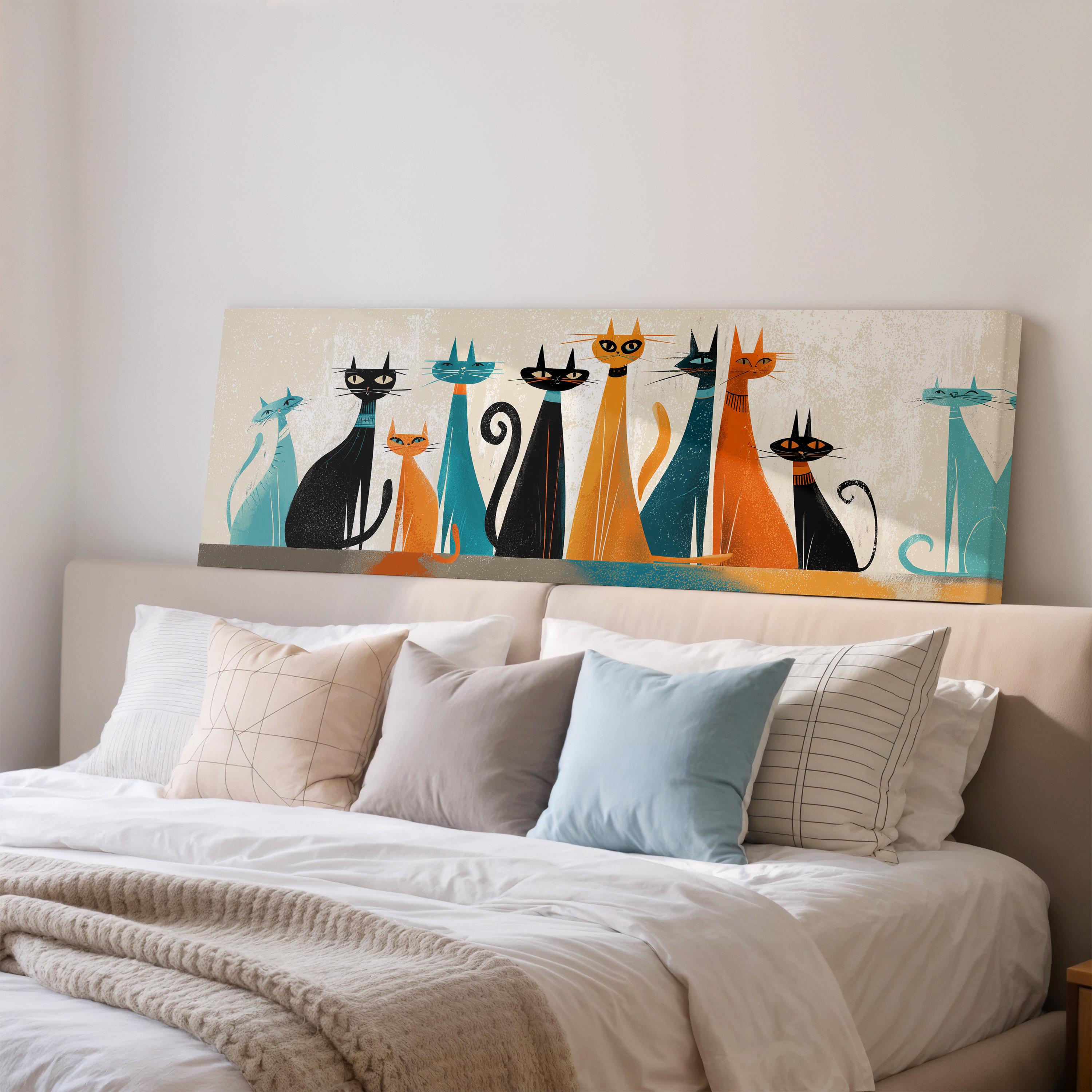 a large bed with a white comforter and a variety of colorful pillows. Above the bed, there is a wall art piece depicting a group of cats in different colors and poses.