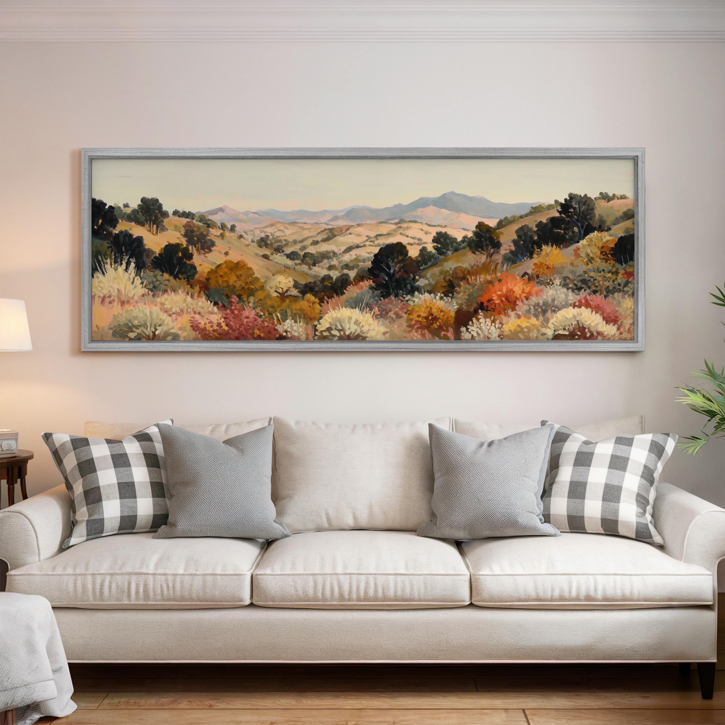 a large, framed painting of a scenic landscape hanging on a wall above a white sofa with gray and white plaid throw pillows.