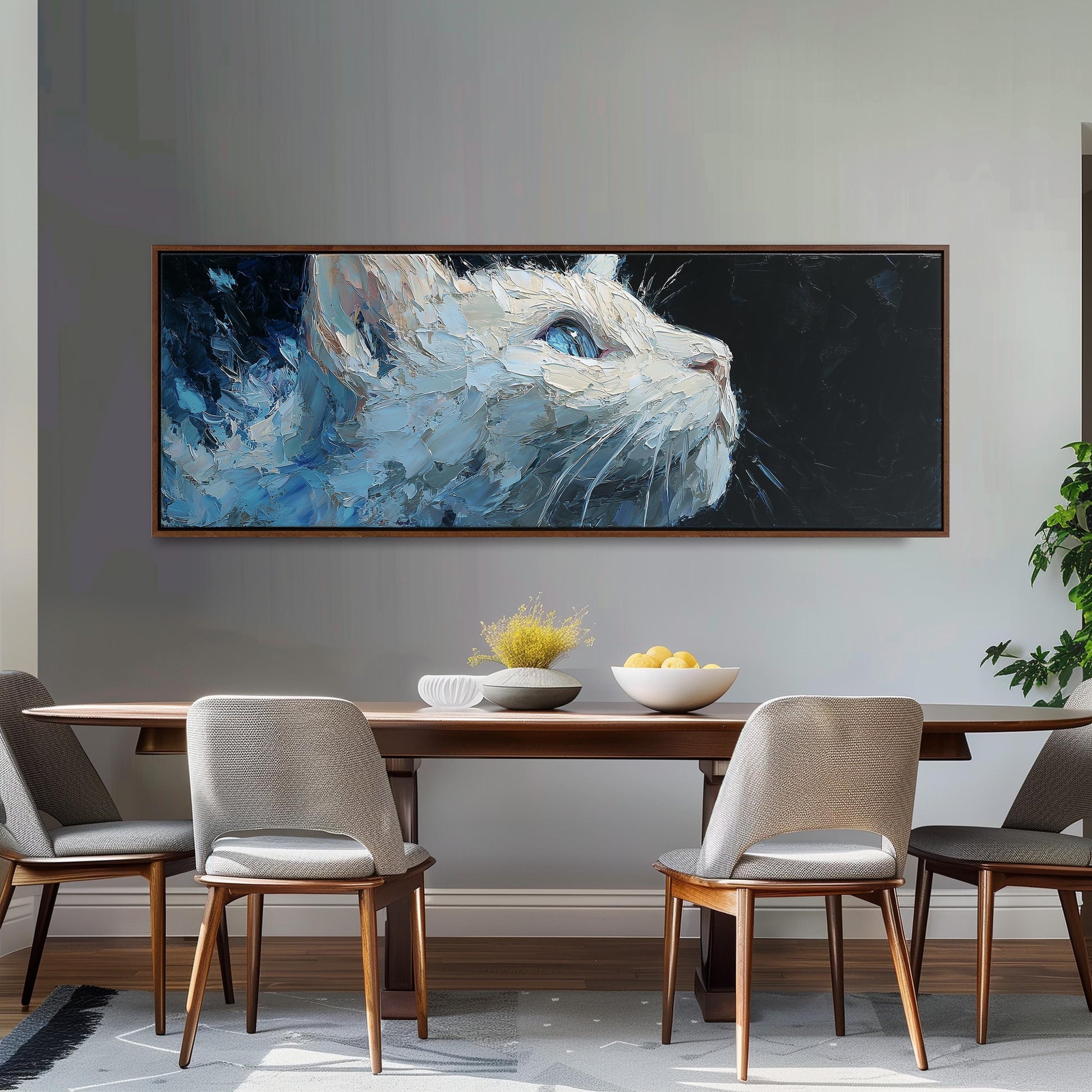 a large painting of a cat's face hanging on a wall above a wooden dining table with four chairs. The table is set with a bowl of fruit and a vase of flowers, creating a cozy and inviting atmosphere.