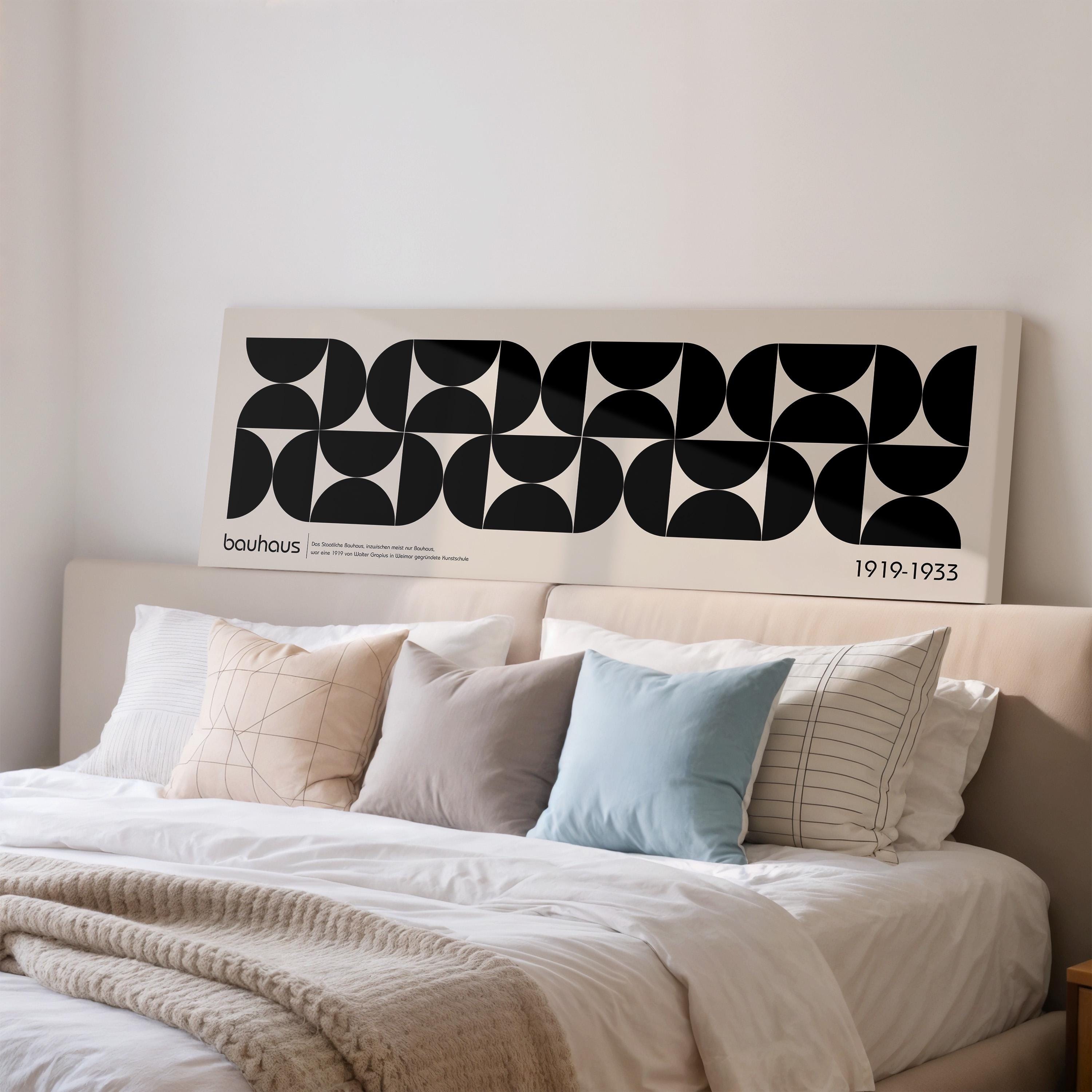 a bedroom with a bed adorned with various pillows and a blanket. Above the bed, there is a large poster or artwork with a geometric design in black and white.