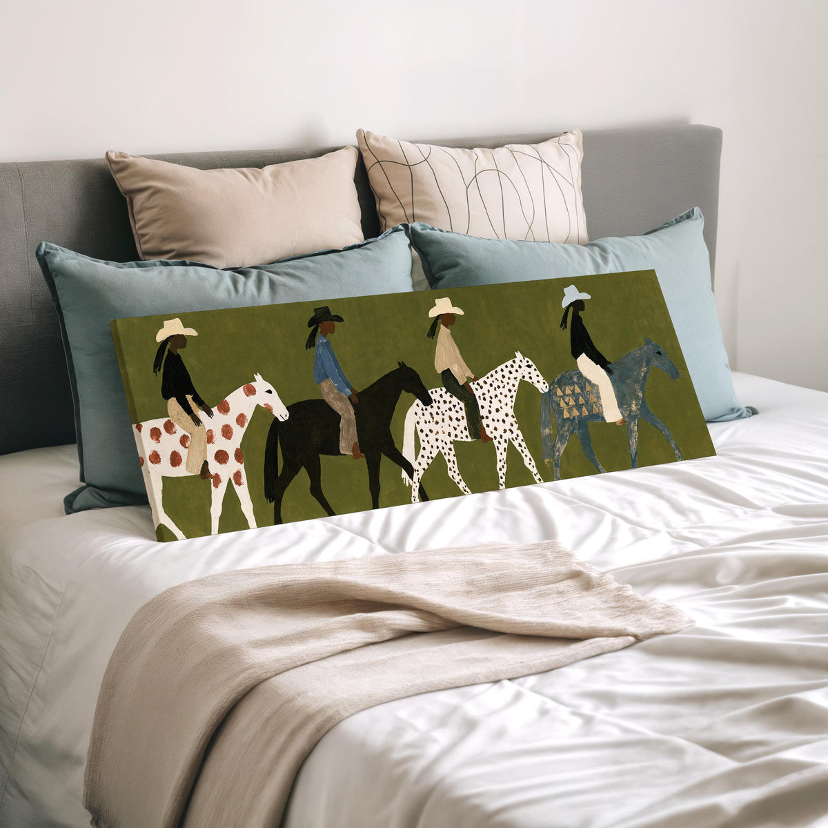 Riders on spotted ponies on olive green wide panoramic canvas print laid on a bed to show its size