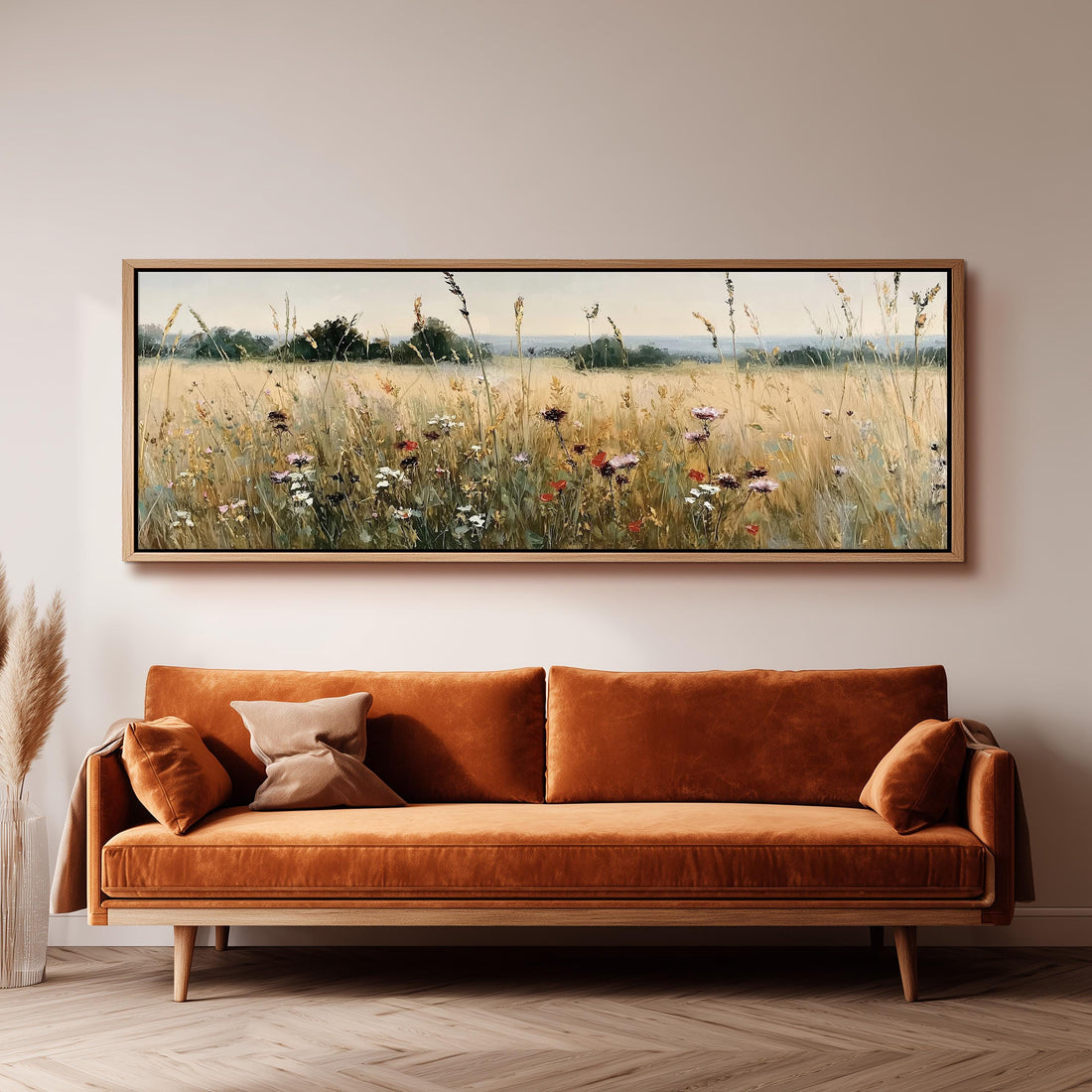 a large, framed painting of a field with tall grass and wildflowers hanging on a wall above a brown sofa.